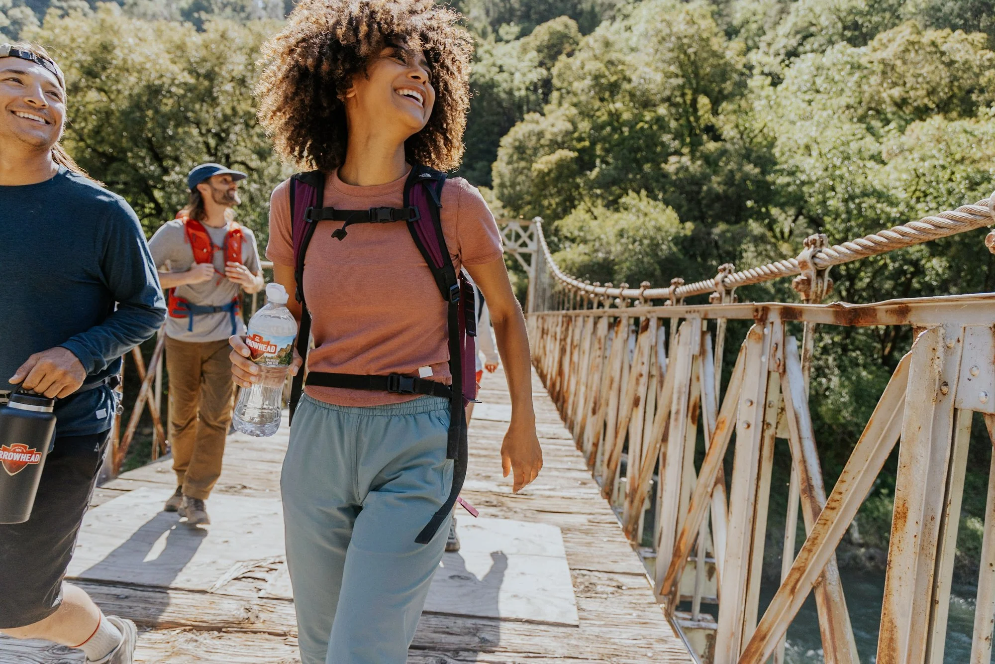 Group of people hiking on a wooden bridge in a forest, smiling and enjoying the outdoors.