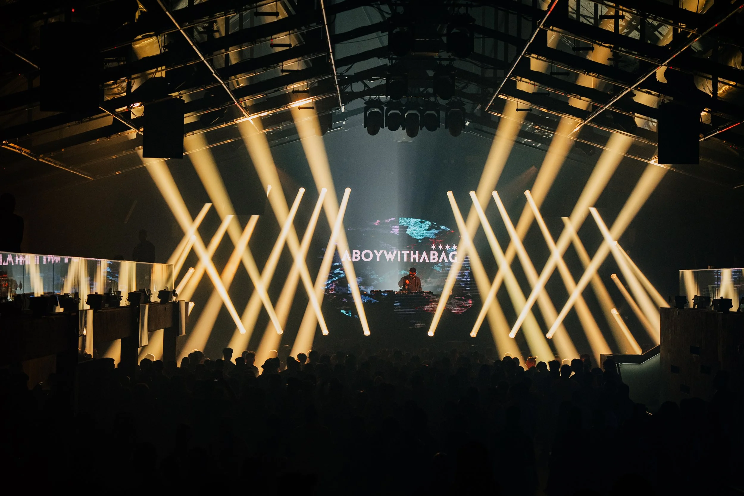 Concert or nightclub scene with stage lights, audience, and a DJ or performer at the front.