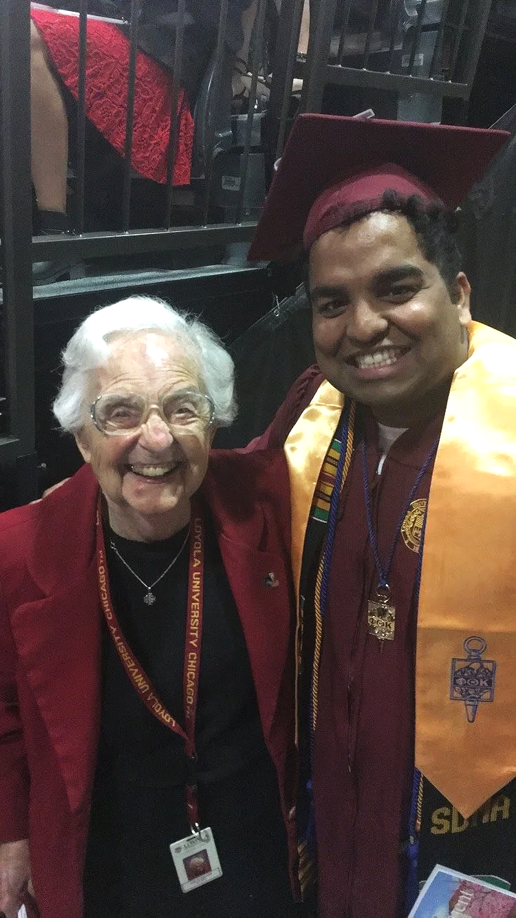 A young man in a maroon graduation gown and cap with a gold stole, standing next to an elderly woman in a red blazer, both smiling at the camera. They are at a graduation ceremony at the University of Chicago.