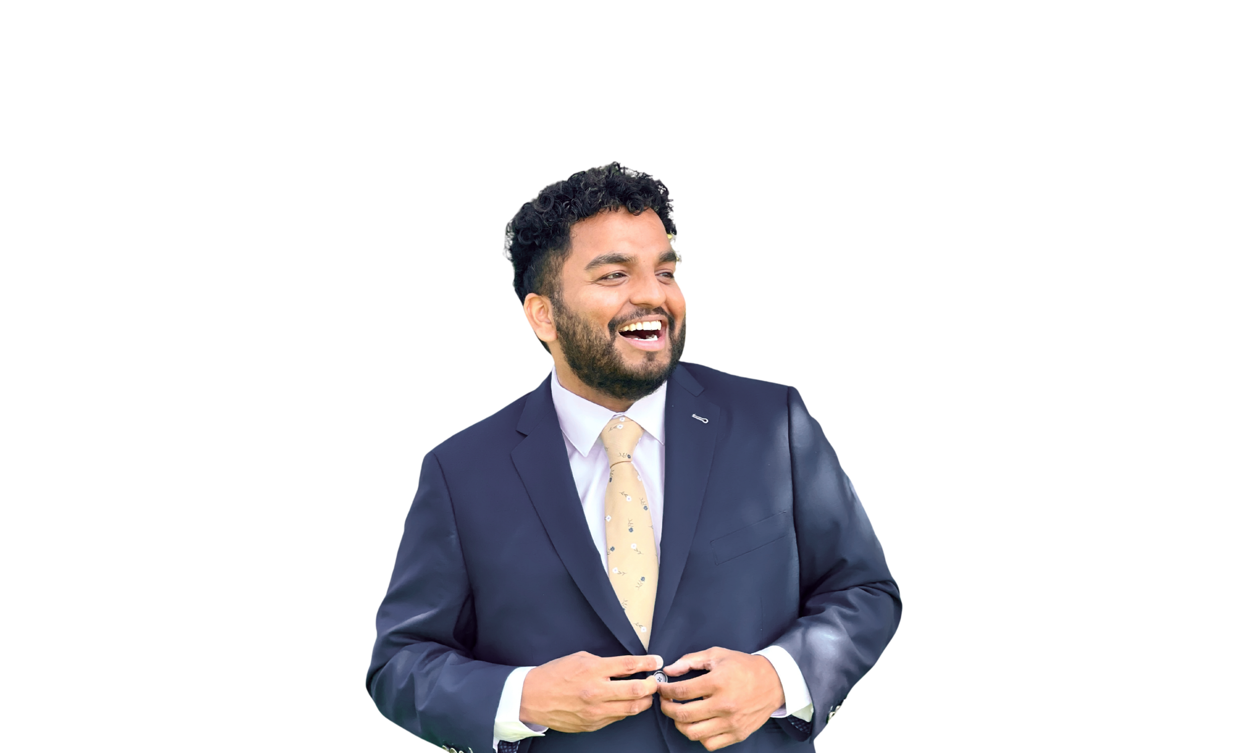 A man with dark curly hair and a beard, dressed in a navy blue suit with a light yellow tie, smiling and looking to his left.