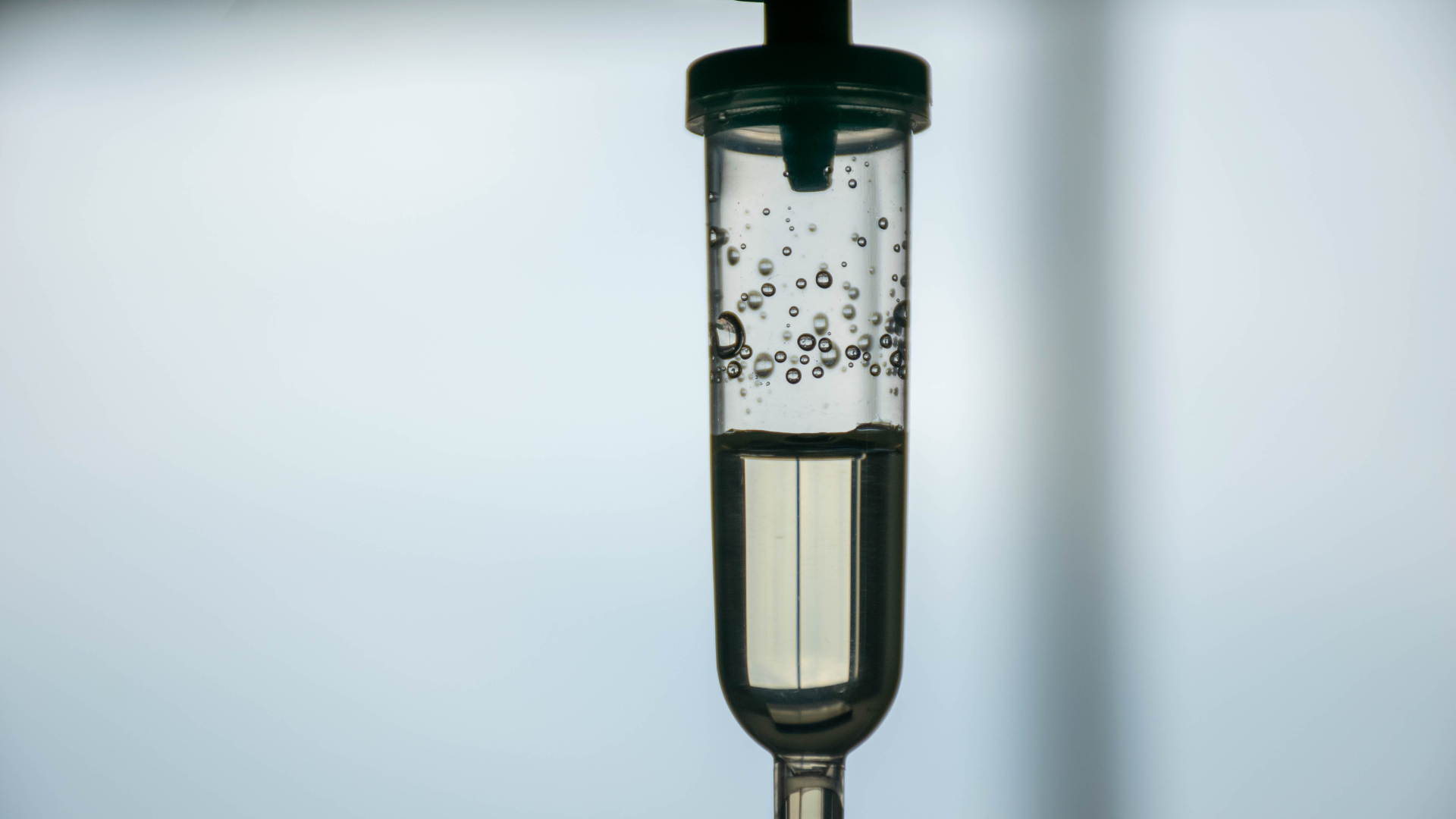 Close-up of a dropper with bubbling, clear liquid inside against a plain background.