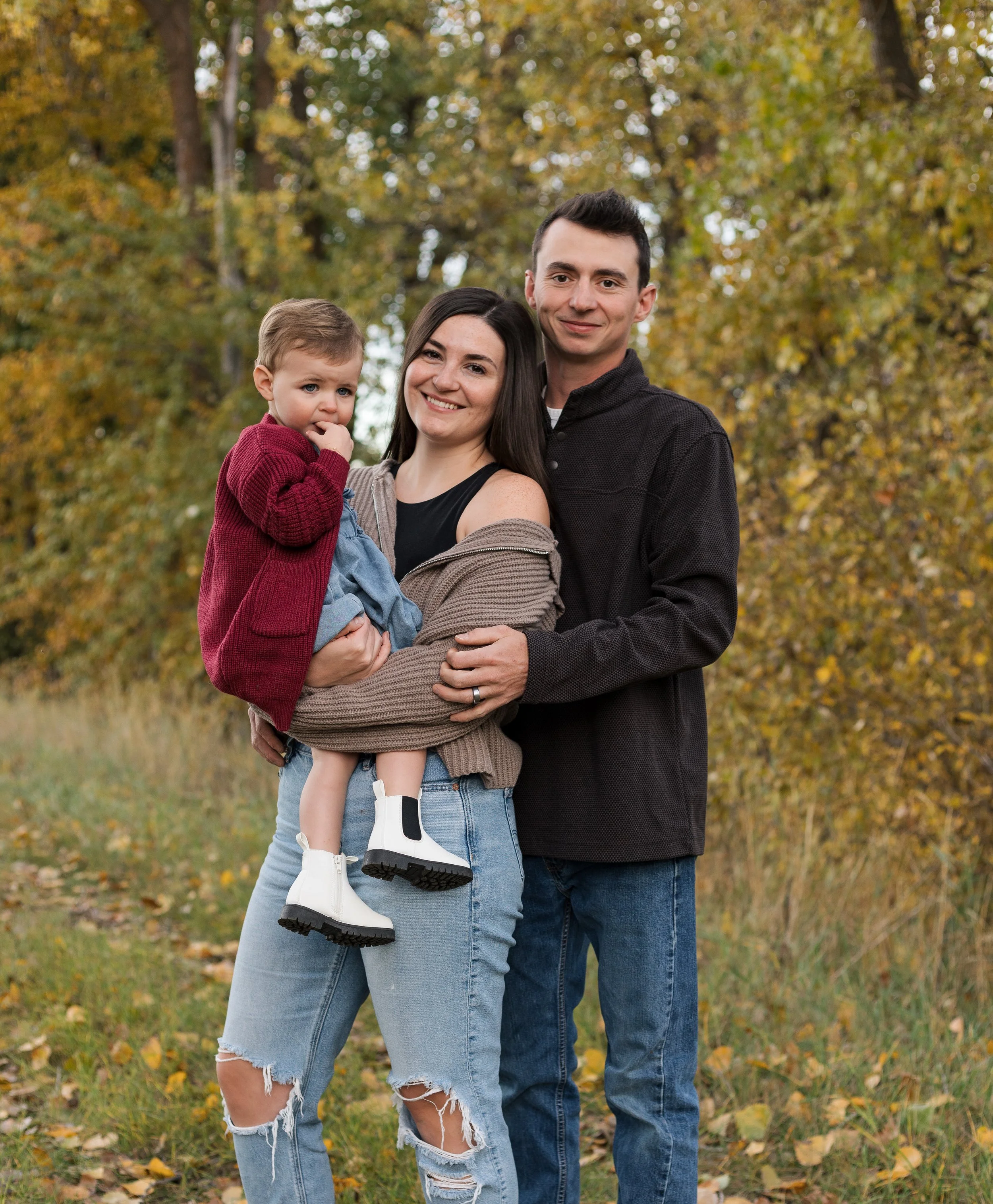 Joslyn and her family standing outdoors in an autumn park with colorful fall foliage, smiling at the camera.