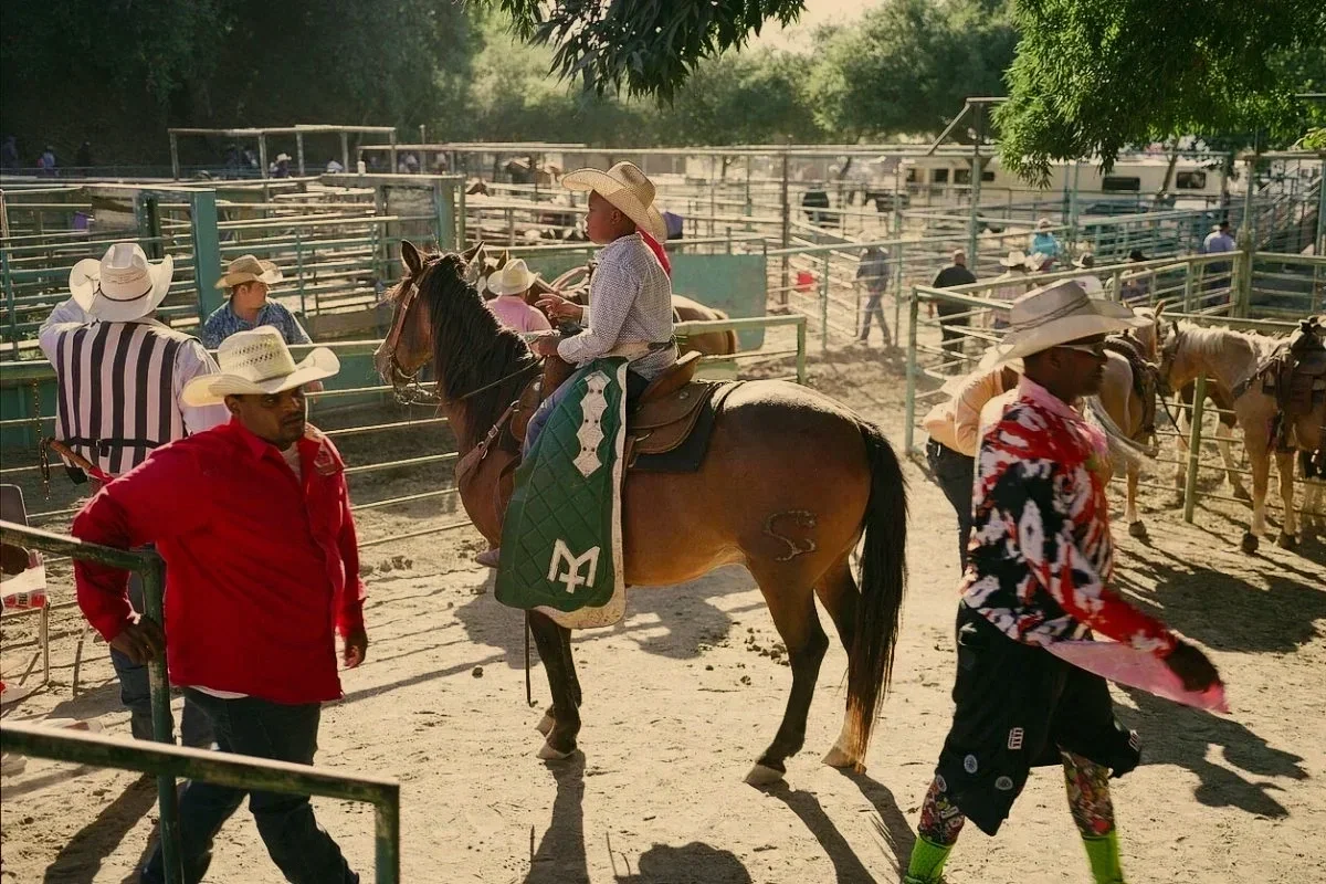 Black cowboys on horseback and people in cowboy hats prepare behind rodeo arena at the Bill Pickett Invitational Rodeo in Oakland, California. Photographed by San Francisco based commercial and editorial photographer, Gabriela Hasbun.
