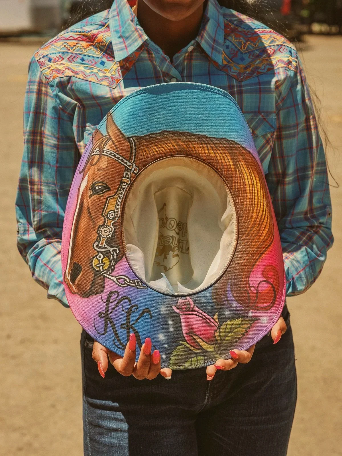 A woman holding a colorful cowboy hat painted with a horse and floral designs.