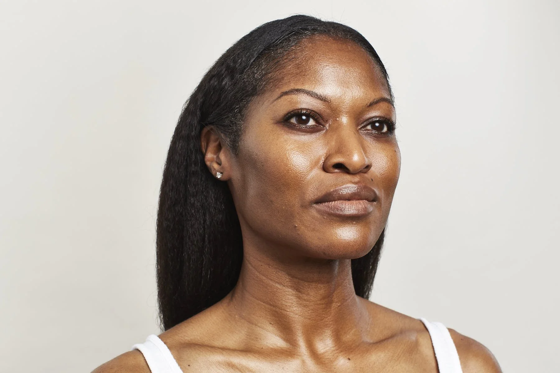 A woman with dark hair, brown eyes, and wearing a white tank top, facing slightly to the right against a plain light background.