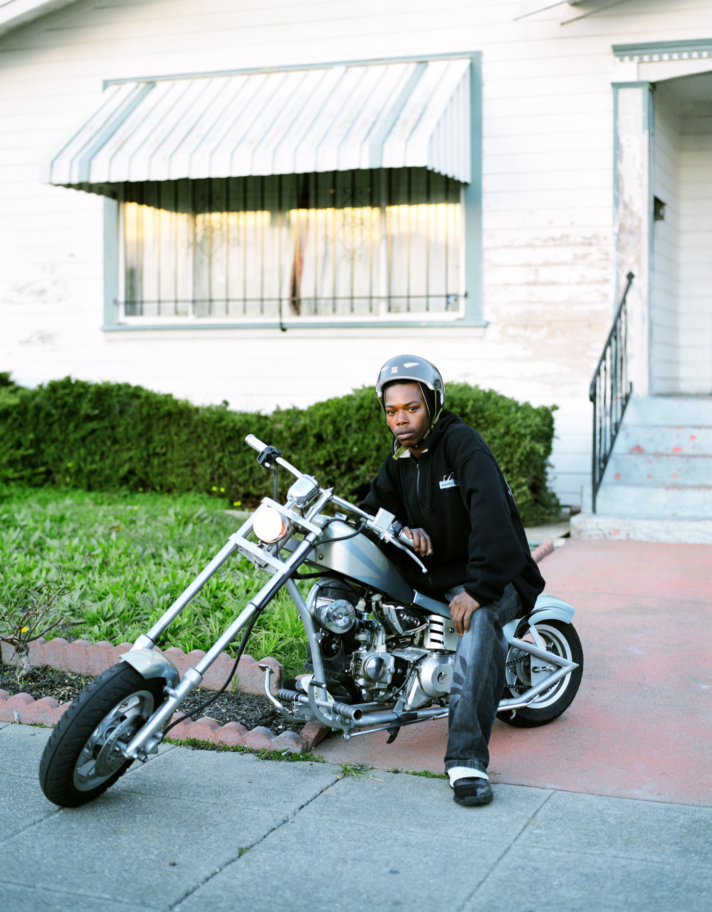 Oakland resident posing with his motorcycle and helmet, photographed by editorial photographer Gabriela Hasbun.