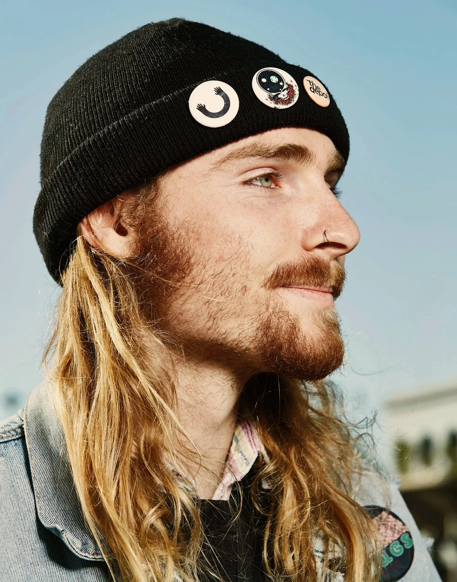 Portrait of skater boy wearing beanie with pins against blue sky.