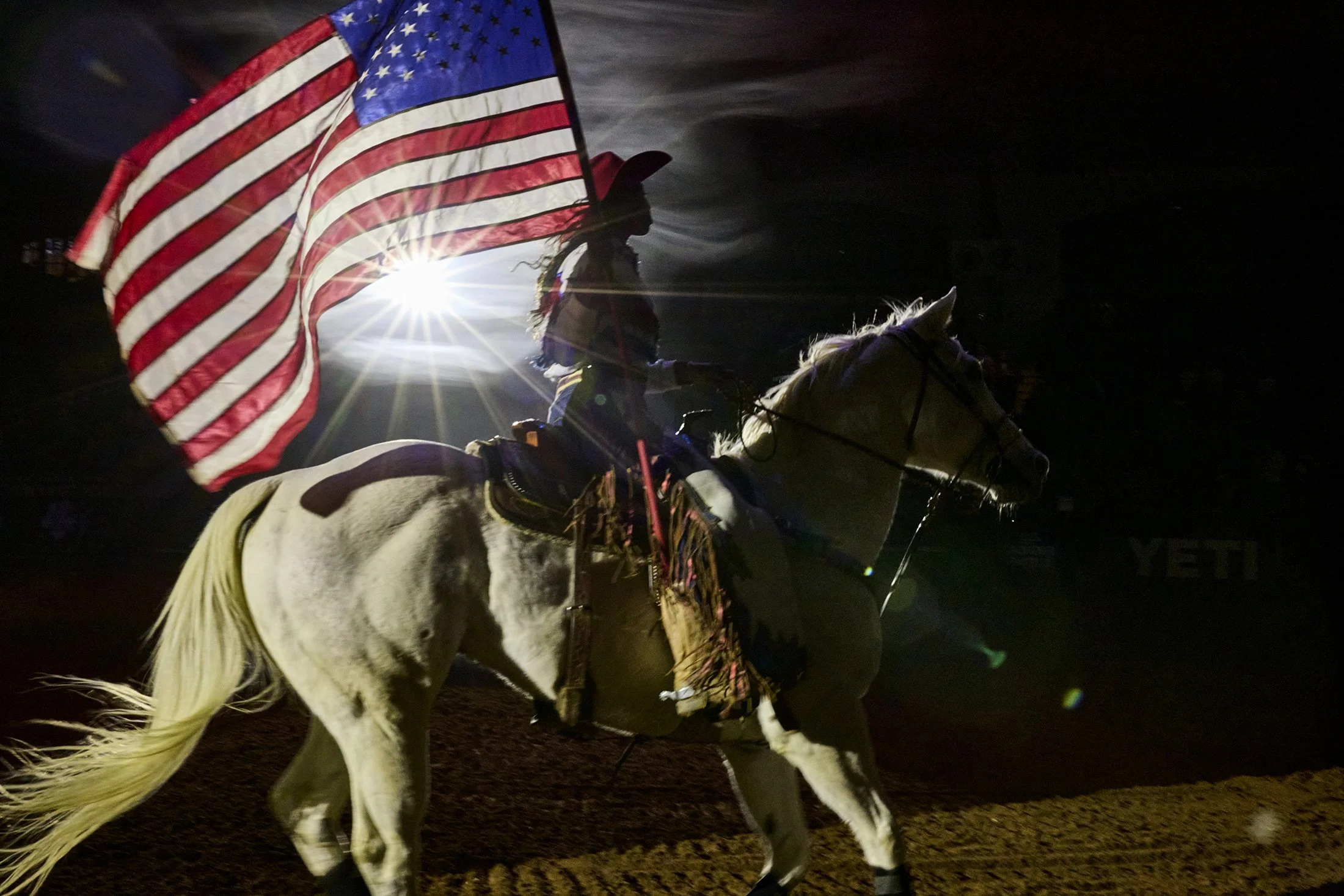 A cowgirl parades the American flag around the arena at the BPIR rodeo in Fort Worth, Tx by Western Photographer Gabriela Hasbun.