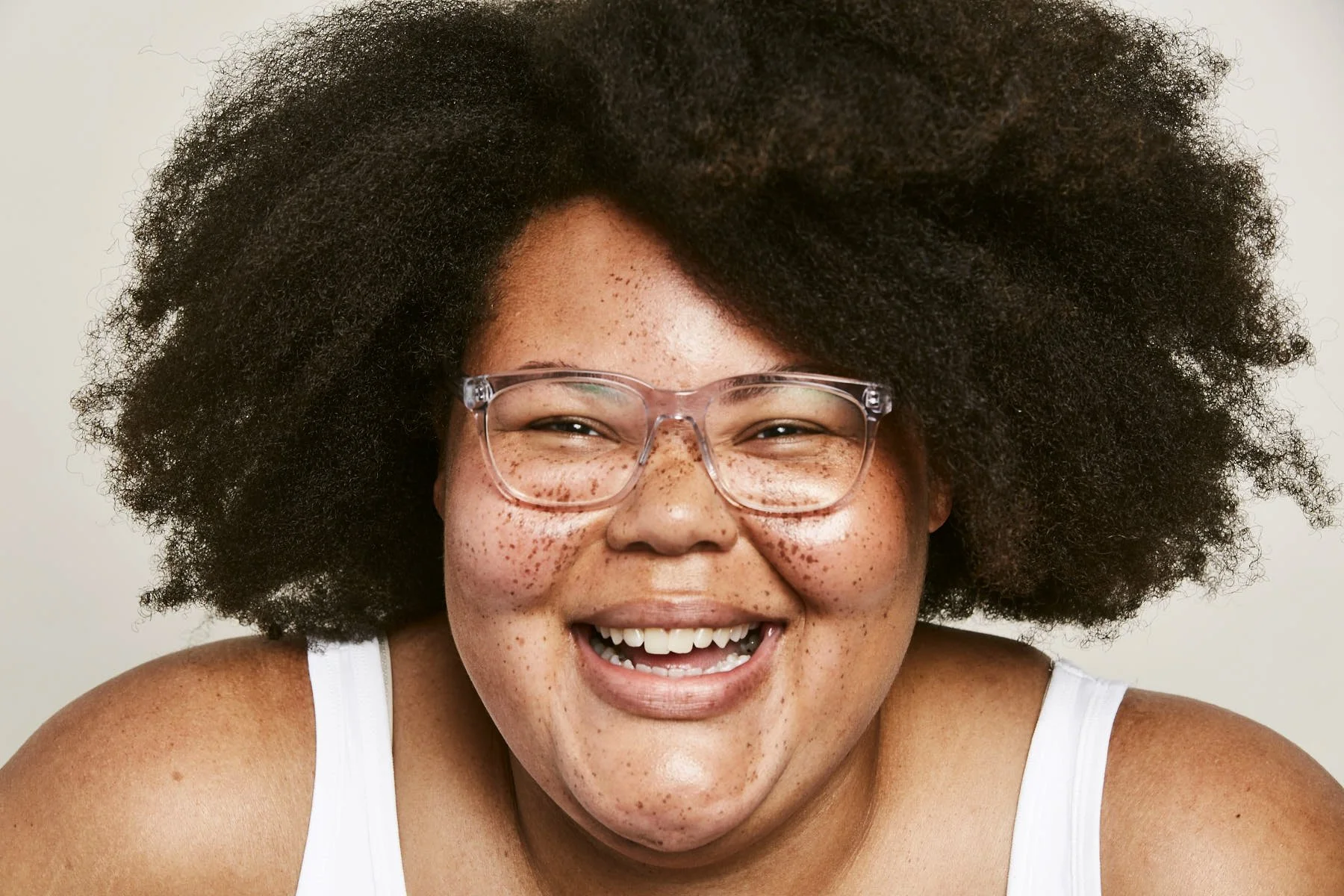 A woman with curly hair, glasses, and freckles smiling brightly.