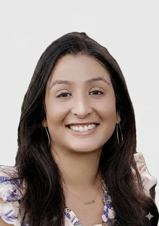 A young woman with long dark hair smiles at the camera, wearing earrings and a patterned top, against a plain background.