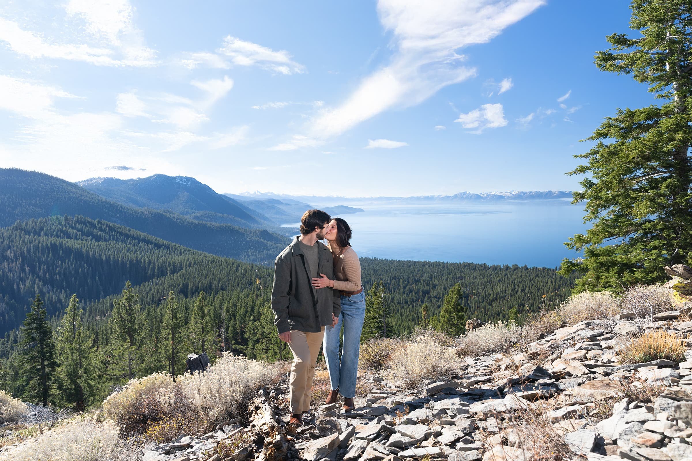 Couple enjoying sunset engagement session on the shore of Lake Tahoe with mountain views.
