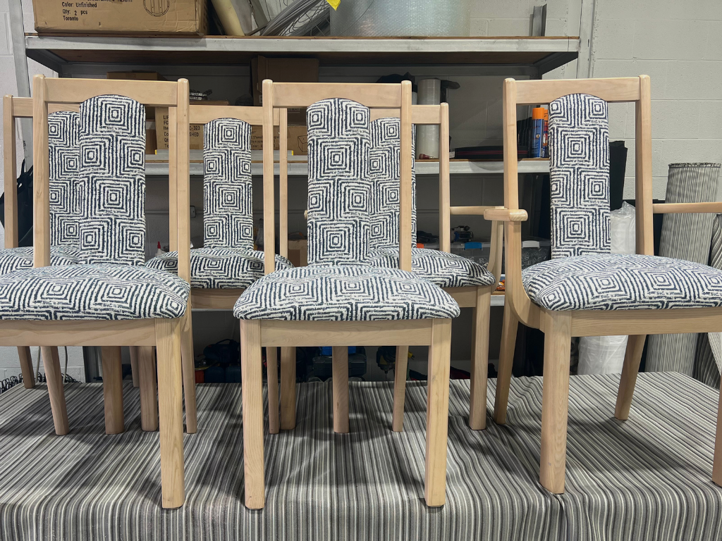 Five wooden chairs with fabric cushions featuring a black and white geometric spiral pattern, placed on a striped surface in a workshop or storage room.