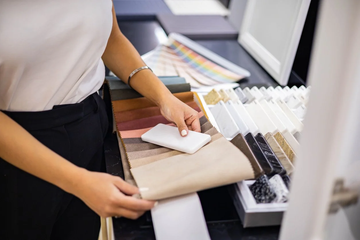Person browsing fabric swatches and color samples on a table in a store.