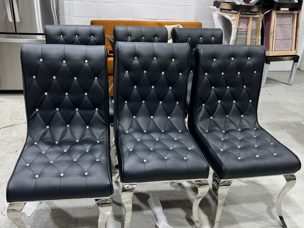 Six black leather chairs with tufted button designs and silver legs, arranged in a row in an indoor setting.