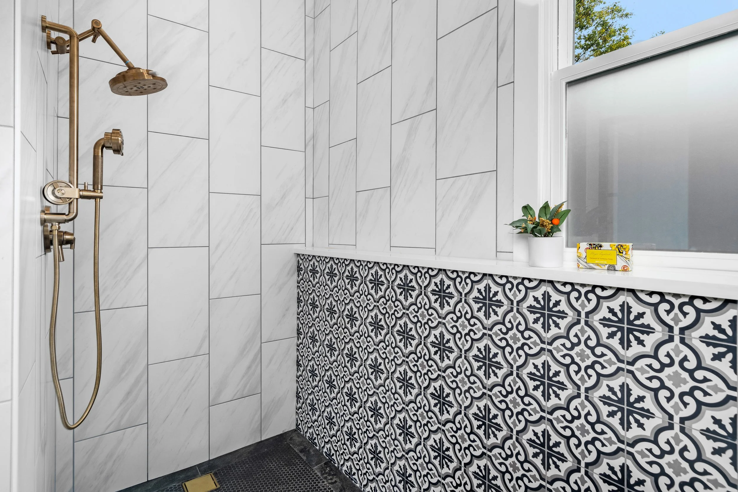 Modern bathroom with patterned black and white tile wall, marble tile walls, black-framed glass partition, window with frosted glass. project by B Group Architecture, Inc.