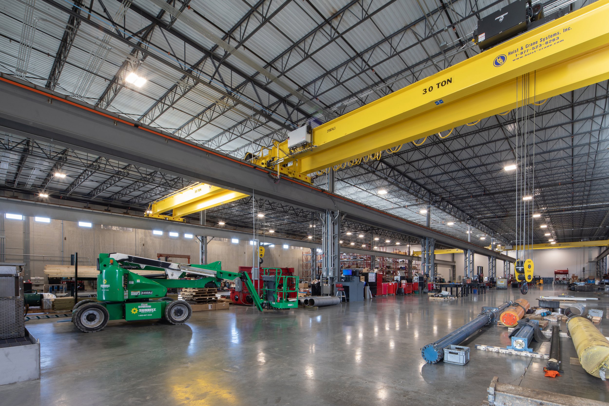 Motion Industries Fluid Power Shop  industrial warehouse with yellow overhead crane systems, construction equipment, and metal pipes on the floor. project by B Group Architecture, Inc.