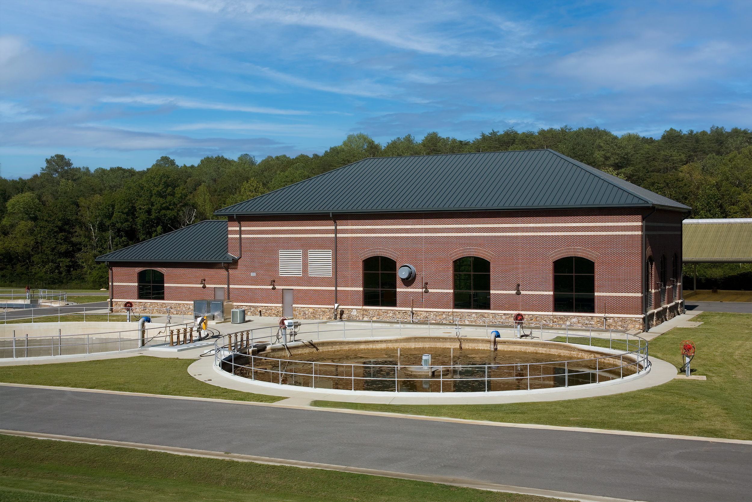 A circular water treatment facility with a brick building, metal railings, and a large water basin at Turkey Creek Wastewater Treatment Plant - project by B Group Architecture, Inc.