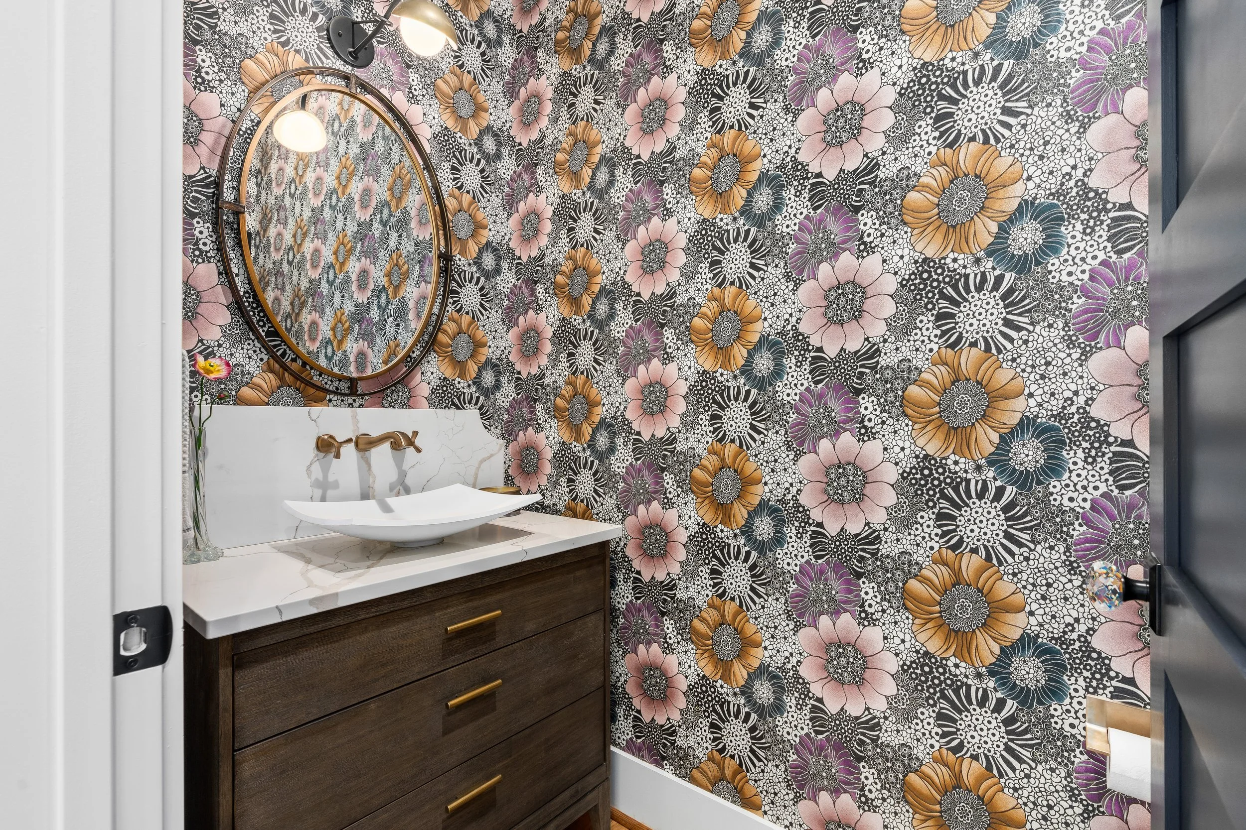 Bathroom with floral patterned wallpaper and a white marble countertop with a vessel sink and gold fixtures. project by B Group Architecture, Inc. 