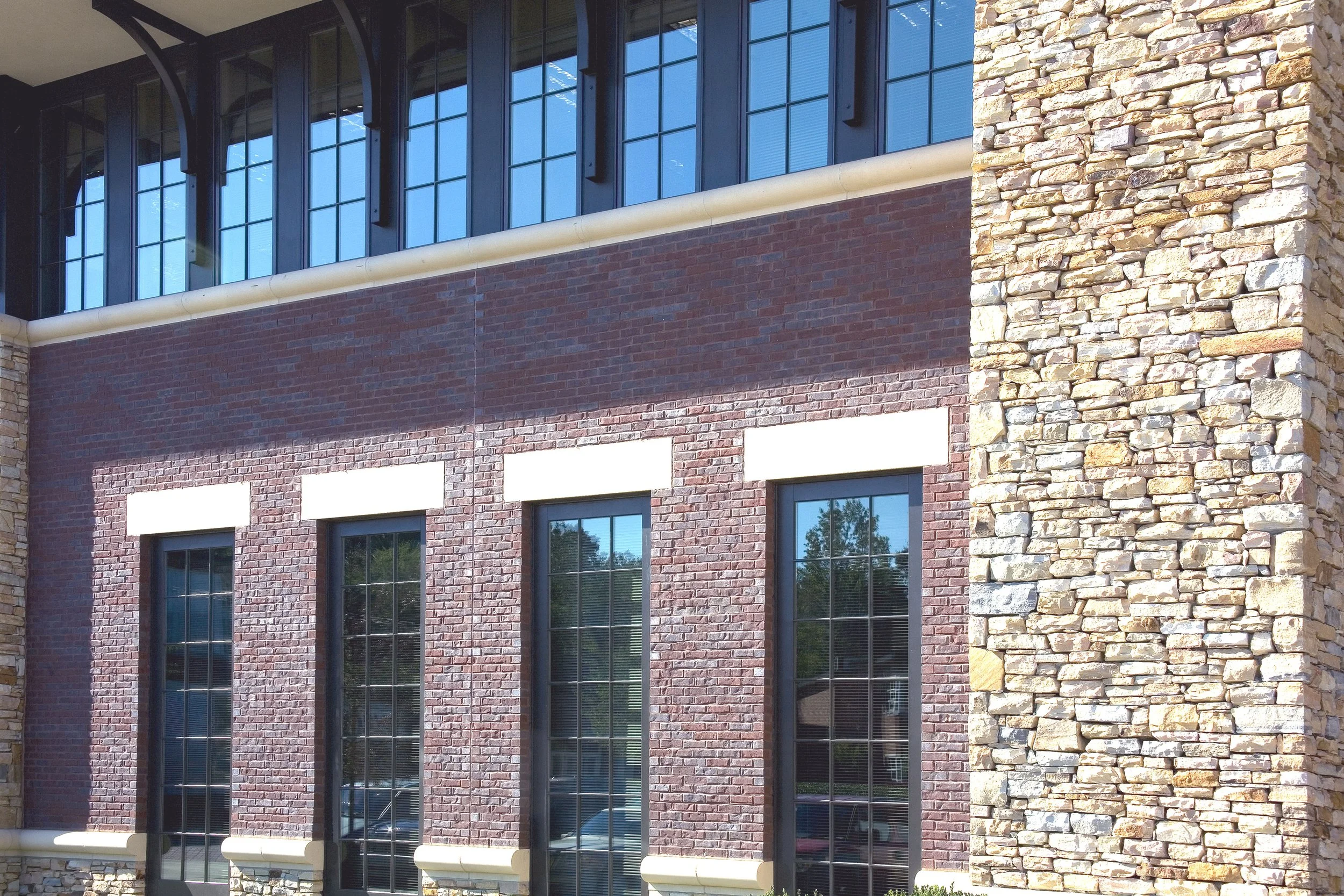 Close-up of a modern building facade with brick and stone exterior, large window panes, and a stone corner detail. project by B Group Architecture, Inc.