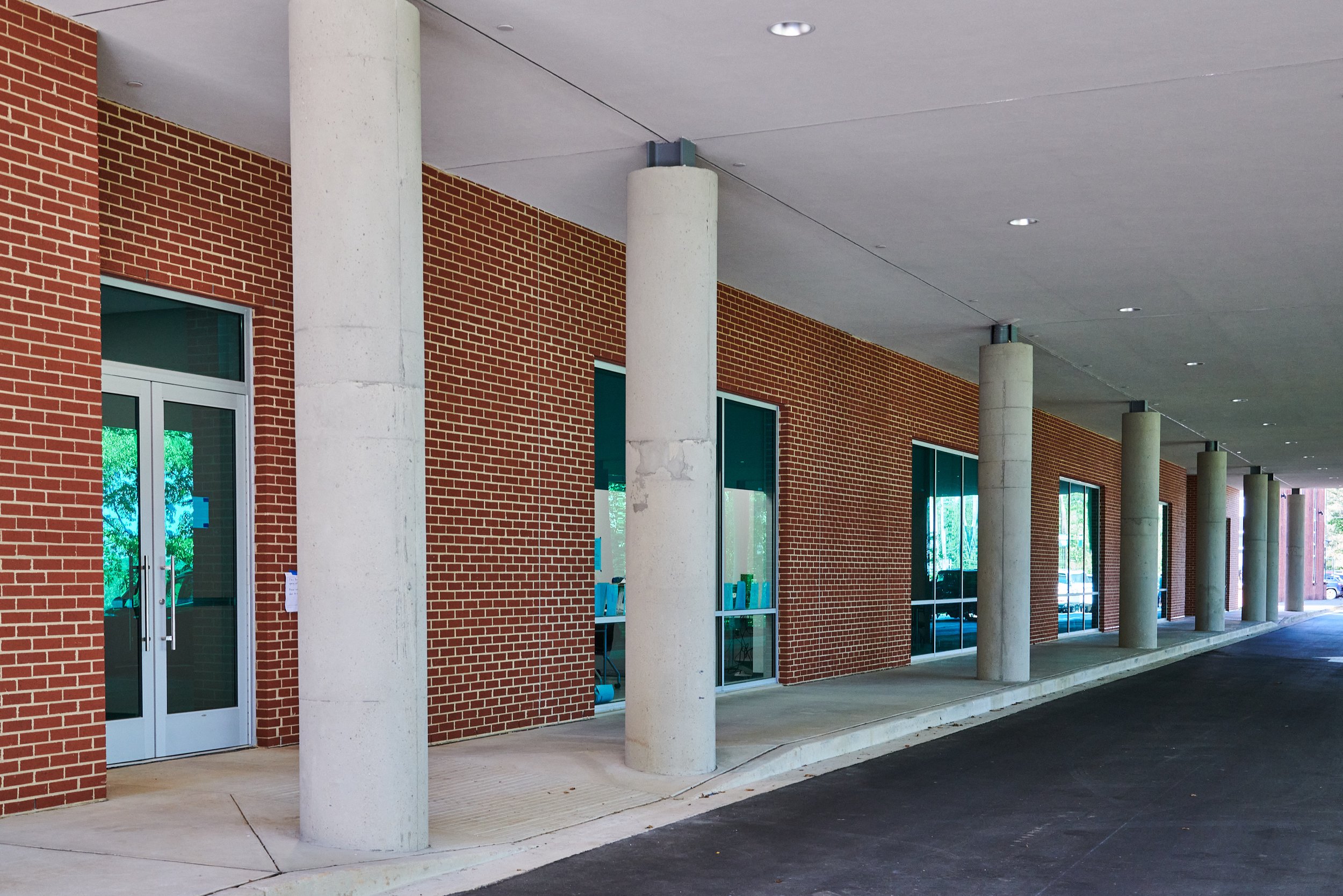 Exterior view of a building with a brick facade, glass windows, concrete columns, and an overhang - project by B Group Architecture, Inc.