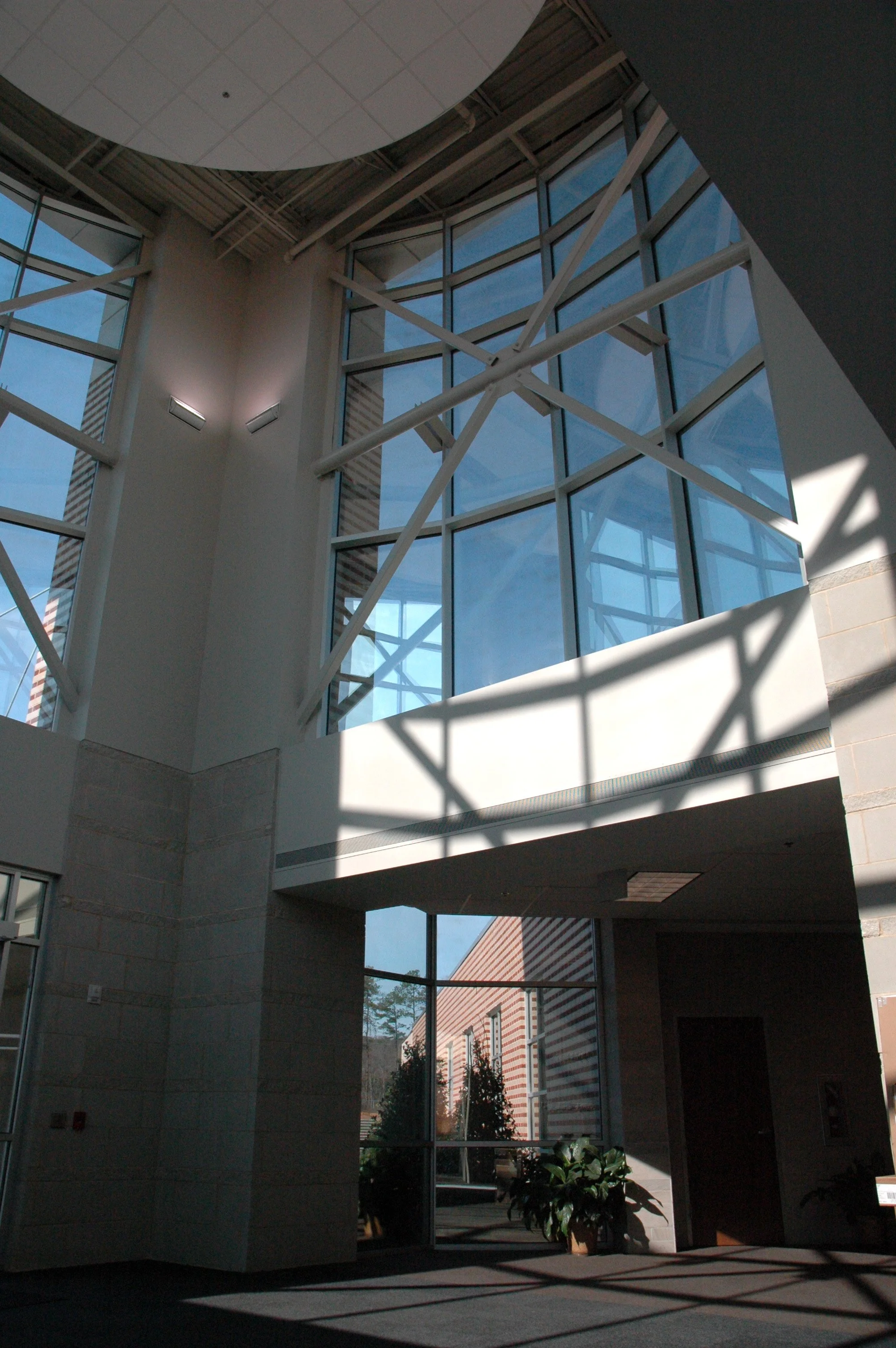 Interior view of the Mountain Brook High School entrance double story space with windows, steel beams, and shadows cast by sunlight pouring into the space.- project by B Group Architecture, Inc.