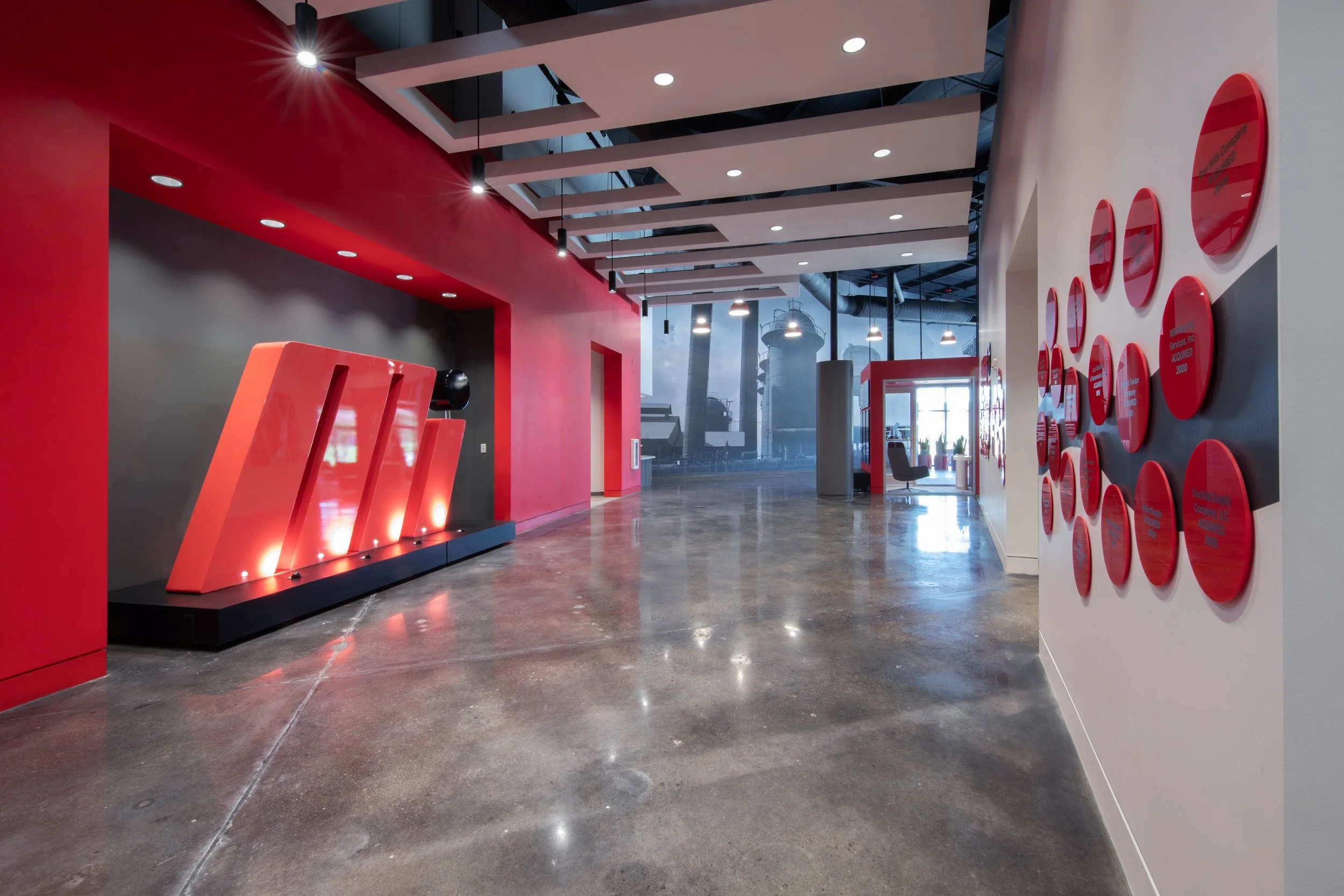 Motion Industries signature red accent wall at a hall leading to a conference room with glass walls, and mural of industrial silos on the wall.  project by B Group Architecture, Inc. 