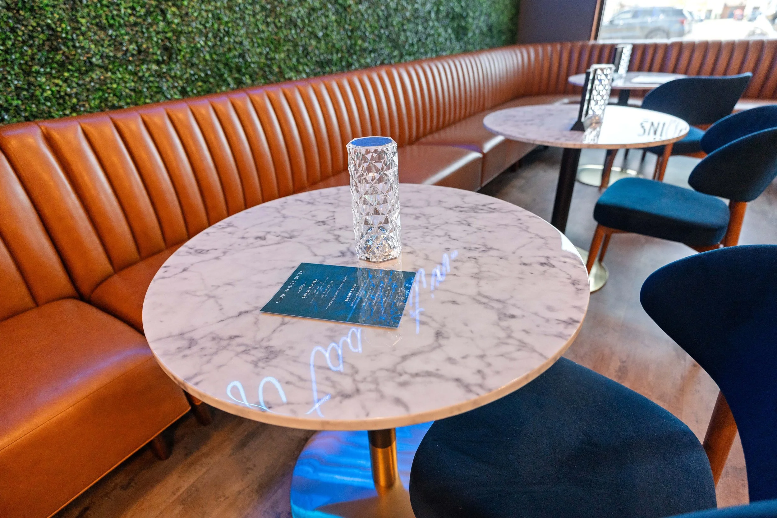 Interior of a restaurant with a marble table, blue velvet chairs, a brown leather banquette seating. project by B Group Architecture, Inc