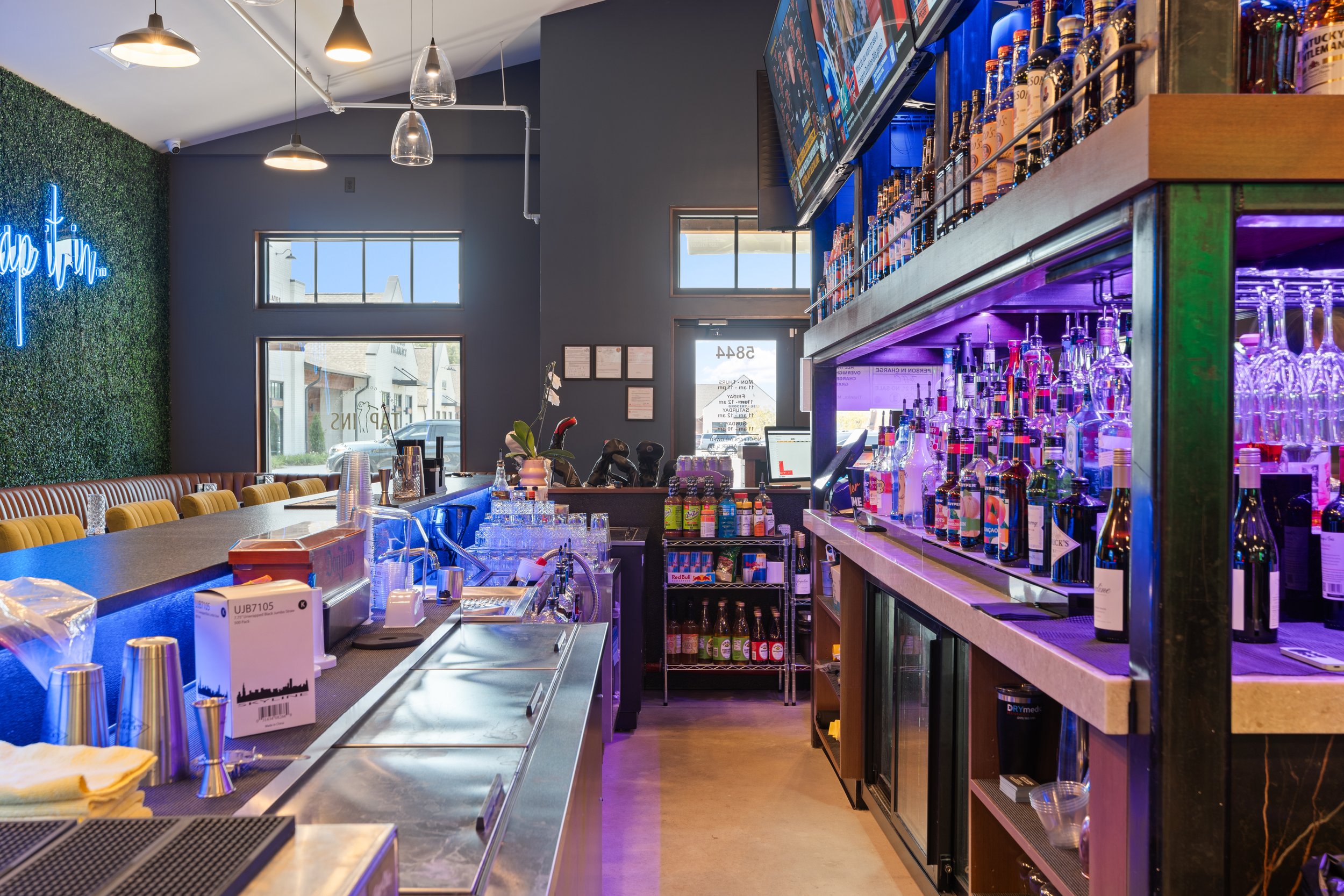 Interior of a modern bar with a long counter, a neon sign on the wall, and plenty of televisions for the sports bar enjoyment. project by B Group Architecture, Inc