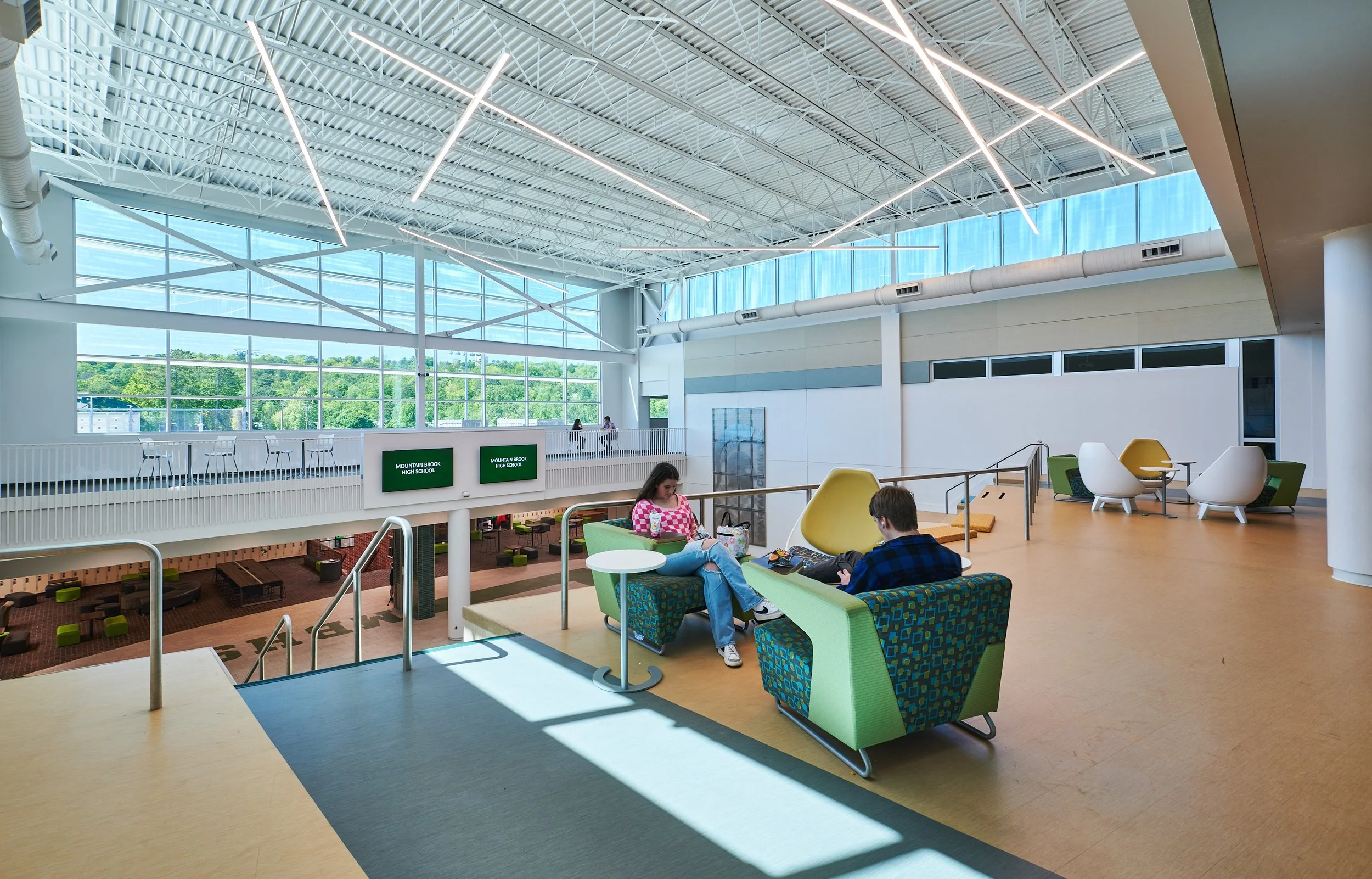 Interior of a modern school lobby with seating area, large windows, and two students sitting and talking- project by B Group Architecture, Inc.