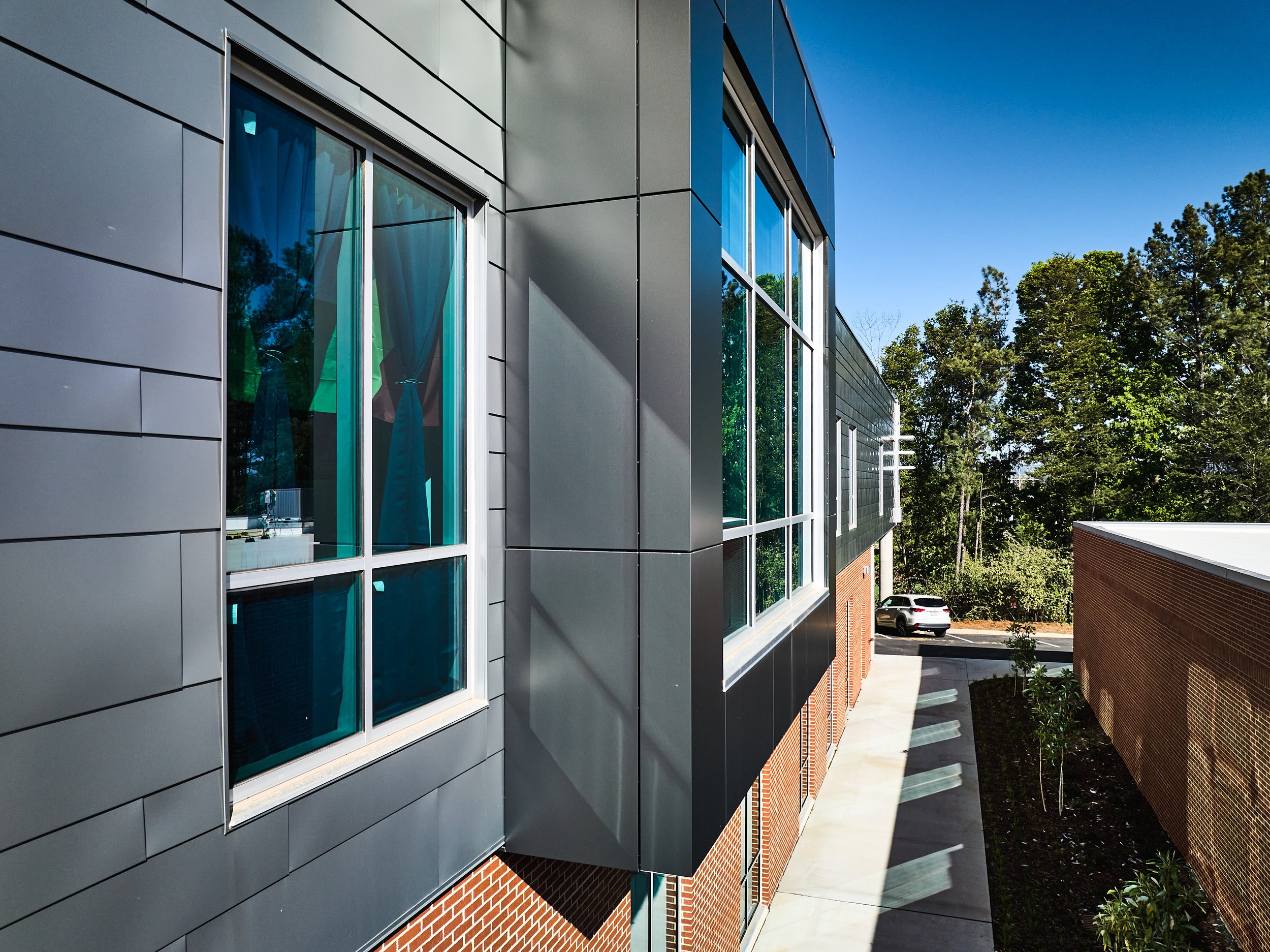 A modern high school with varying sized lapped and seamed metal siding along side of pre-finished composite metal panels and greenish hue glazing- project by B Group Architecture, Inc.