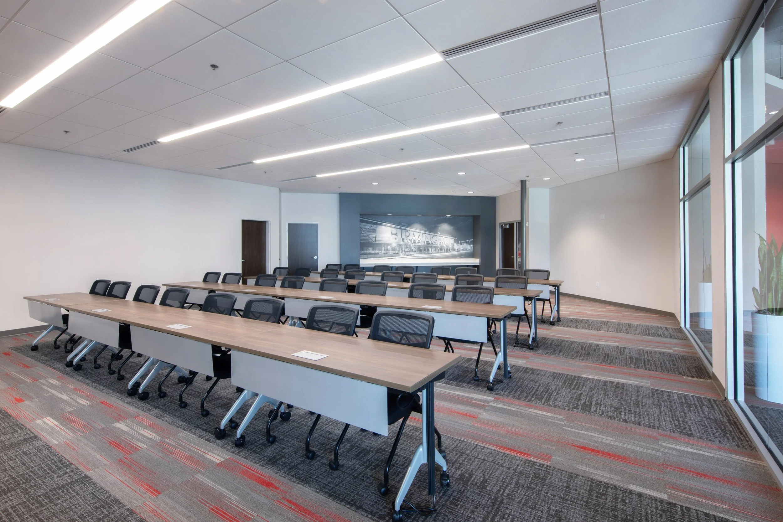 Modern conference room with long tables, black chairs, large windows, and a mural in the background. Carpet brings in corporate colors of Motion Industries.  project by B Group Architecture, Inc. 