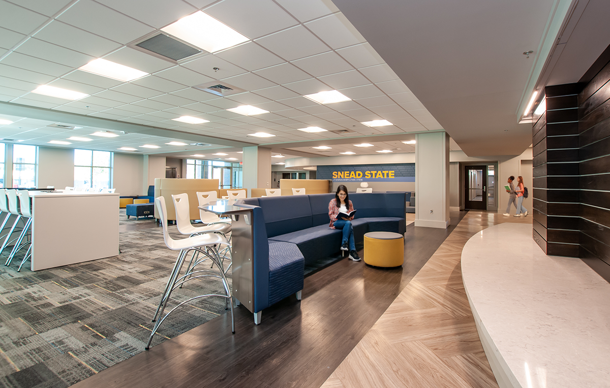 A spacious college lounge at Snead State with modern chairs, a blue curved seating area, and contrasting flooring materials. 