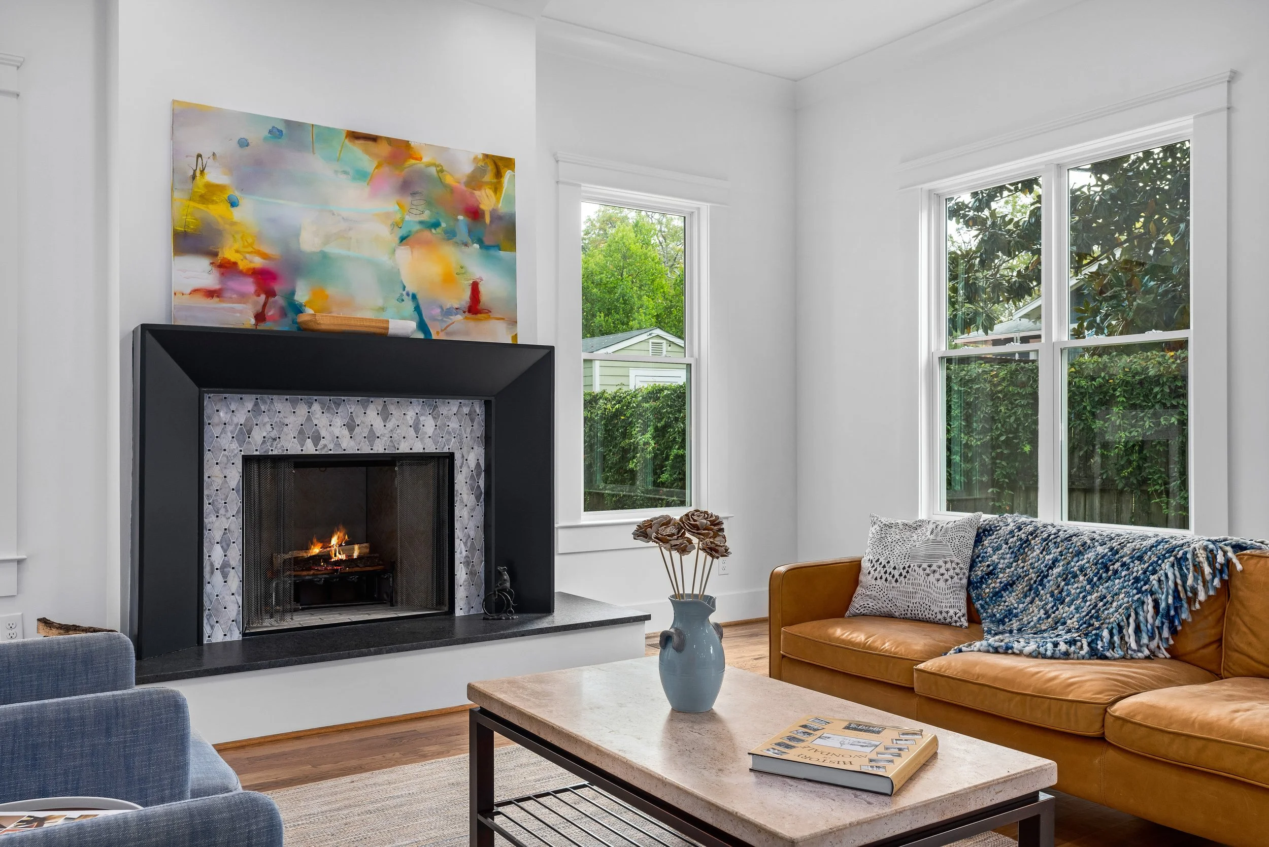 Living room with a white wall, large windows allowing natural light to shine in. The historic fireplace was renovated with tile and contemporary furniture. project by B Group Architecture, Inc.