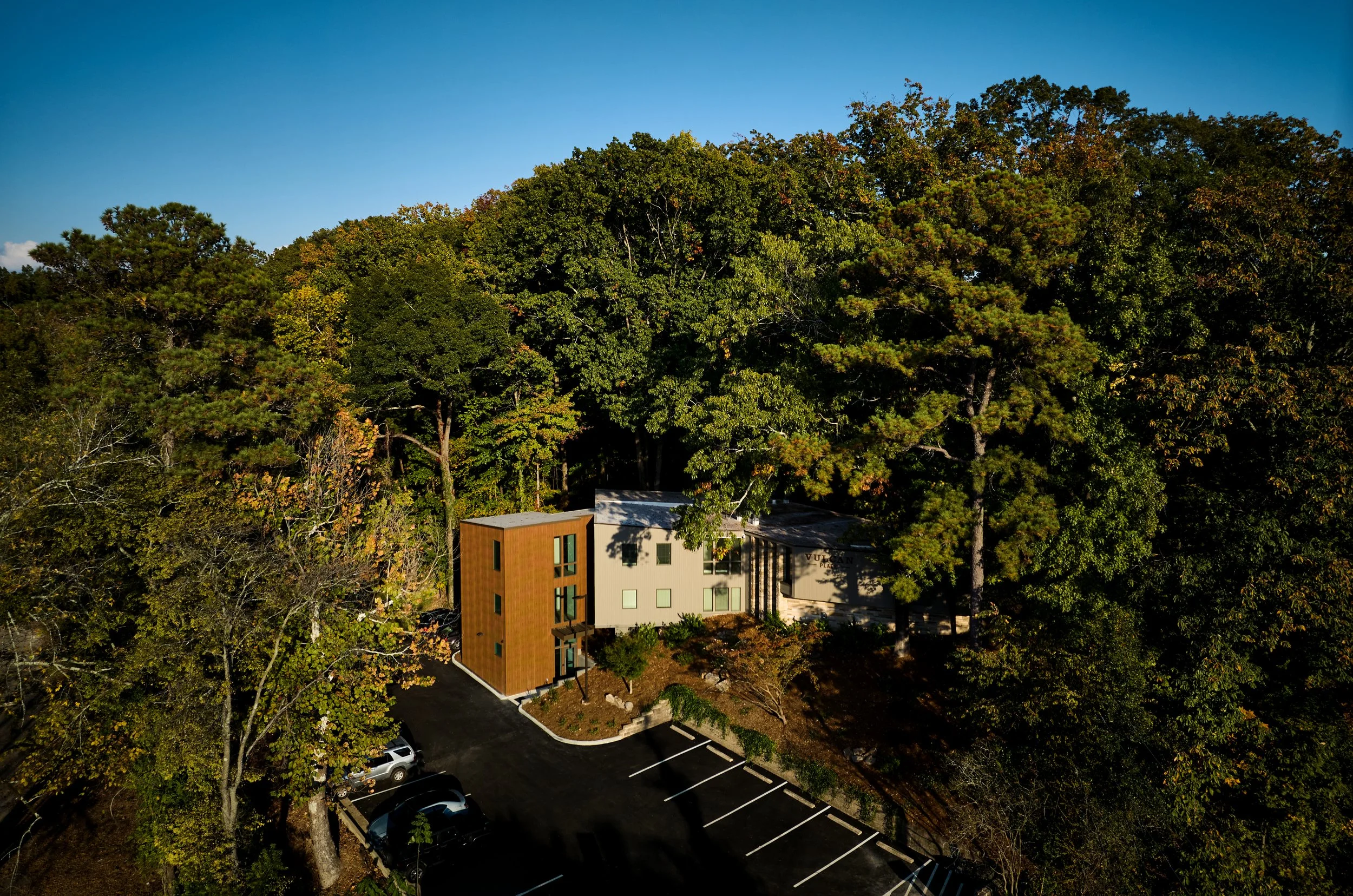 A modern, multi-story building at Vulcan Place in Birmingham, AL surrounded by tall trees in a wooded area. project by B Group Architecture, Inc.