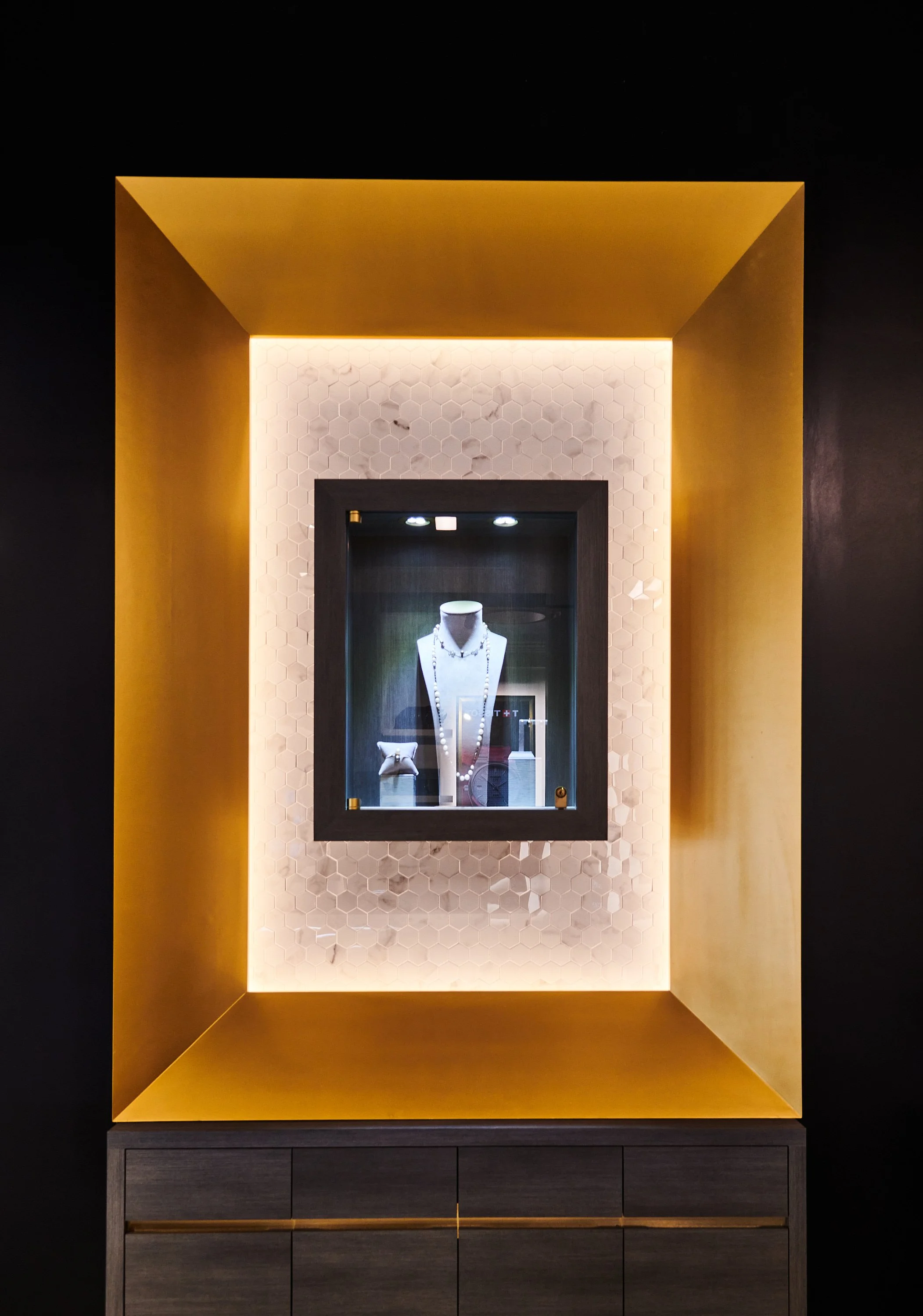 Jewelry display case with chamfered gold accent frame and marble tile accentuating the jewelry housed inside. project by B Group Architecture, Inc 