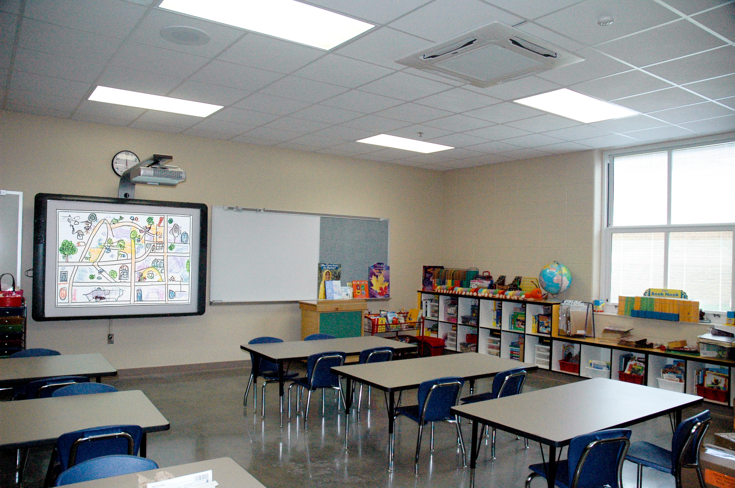 Classroom with tables and chairs, bulletin boards, bookshelf with books, globe, and a large window. - project by B Group Architecture, Inc.