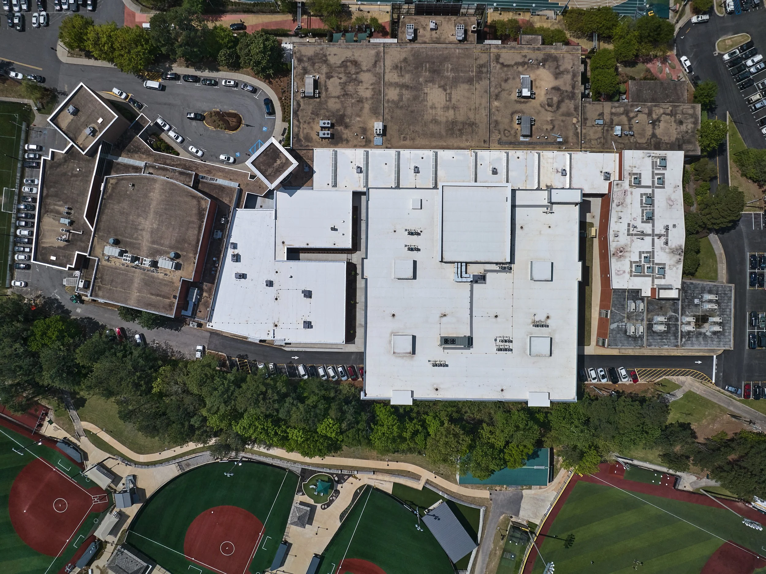 An aerial view of a large high school addition  infill with sports field below. The school has multiple flat roofs, parking lots, and surrounding trees- project by B Group Architecture, Inc.