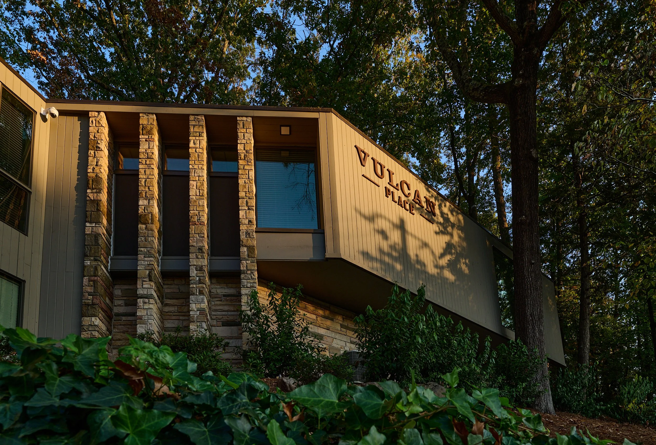 Exterior of a residential building with a sign reading 'Vulgare Place', surrounded by trees and greenery, during daylight.