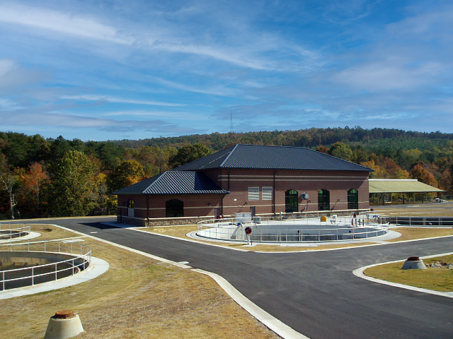 A circular water treatment facility with a brick building, metal railings, and a large water basin at Turkey Creek Wastewater Treatment Plant - project by B Group Architecture, Inc.