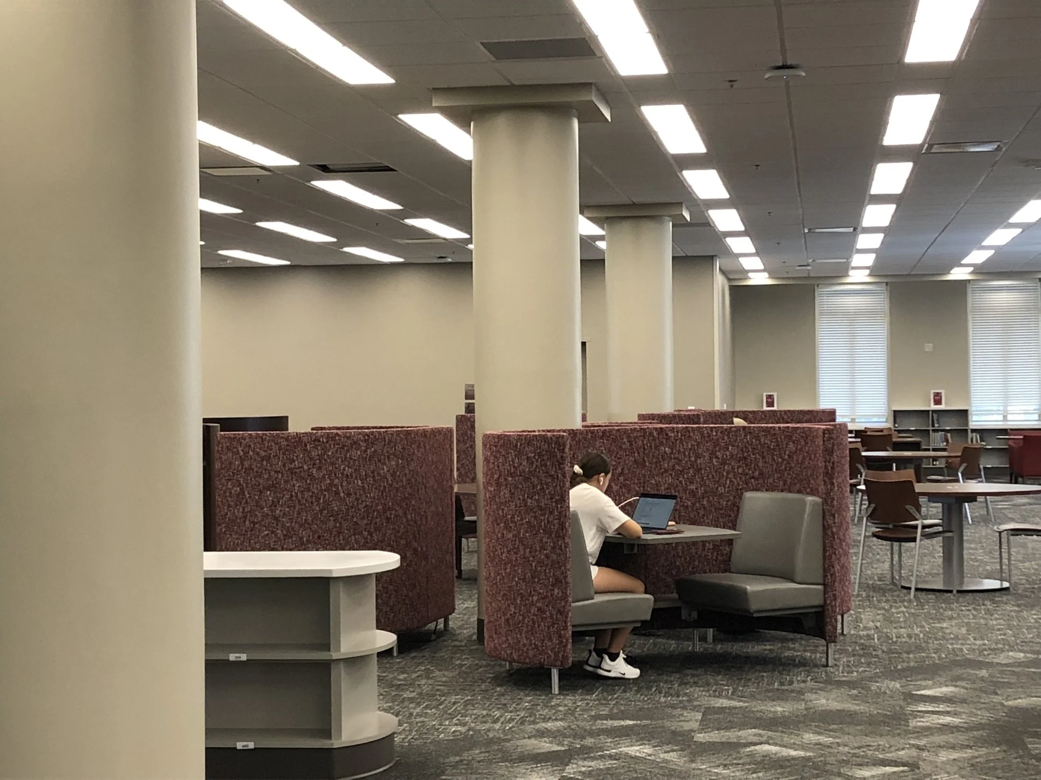 An interior view of library seating with red upholstered chairs equipped with small wooden tablet arms lights visible in the background - project by B Group Architecture, Inc