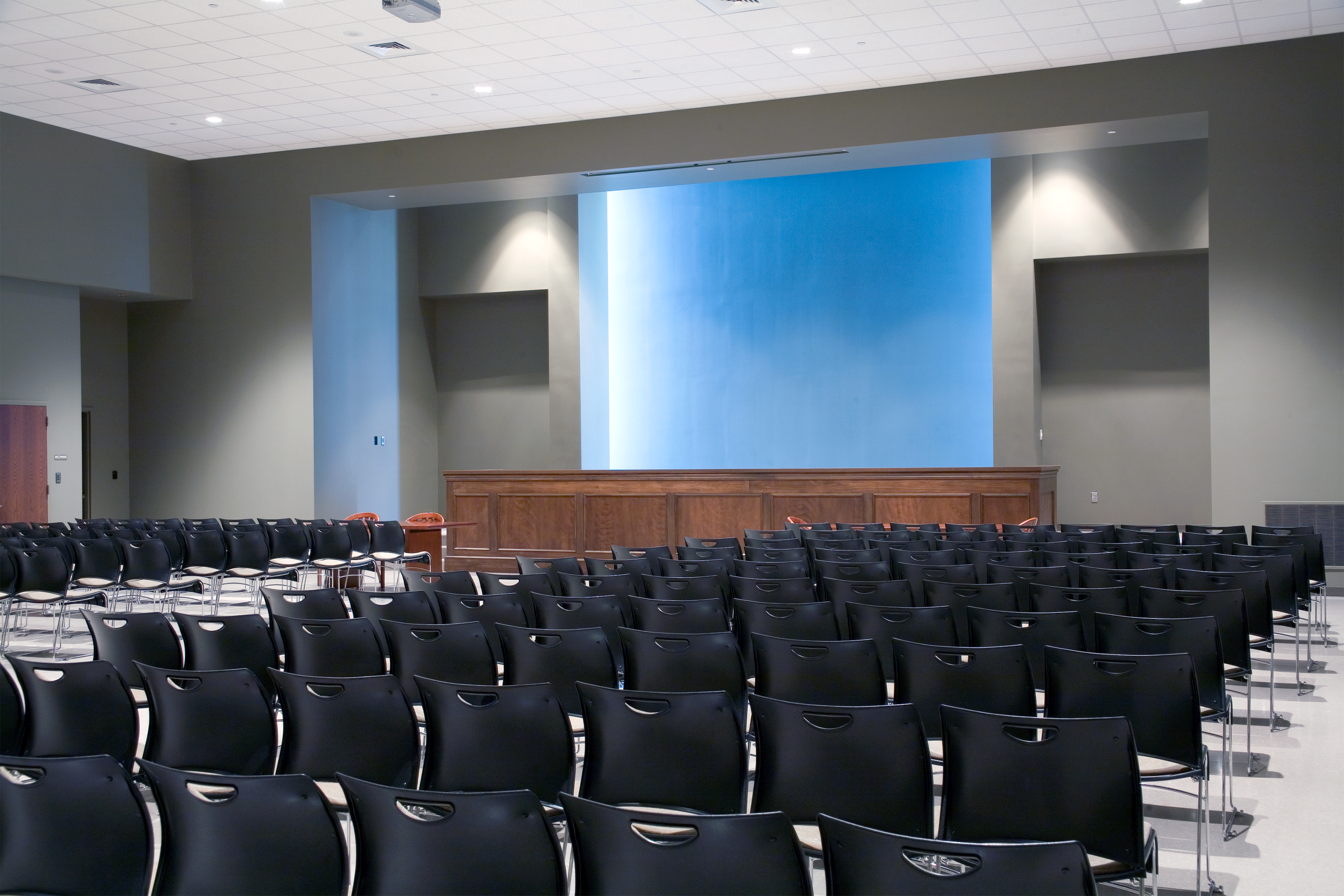 Pelham, AL Police Department's conference or event room with chairs facing a stage with a blue backdrop and wooden paneling. project by B Group Architecture Inc.