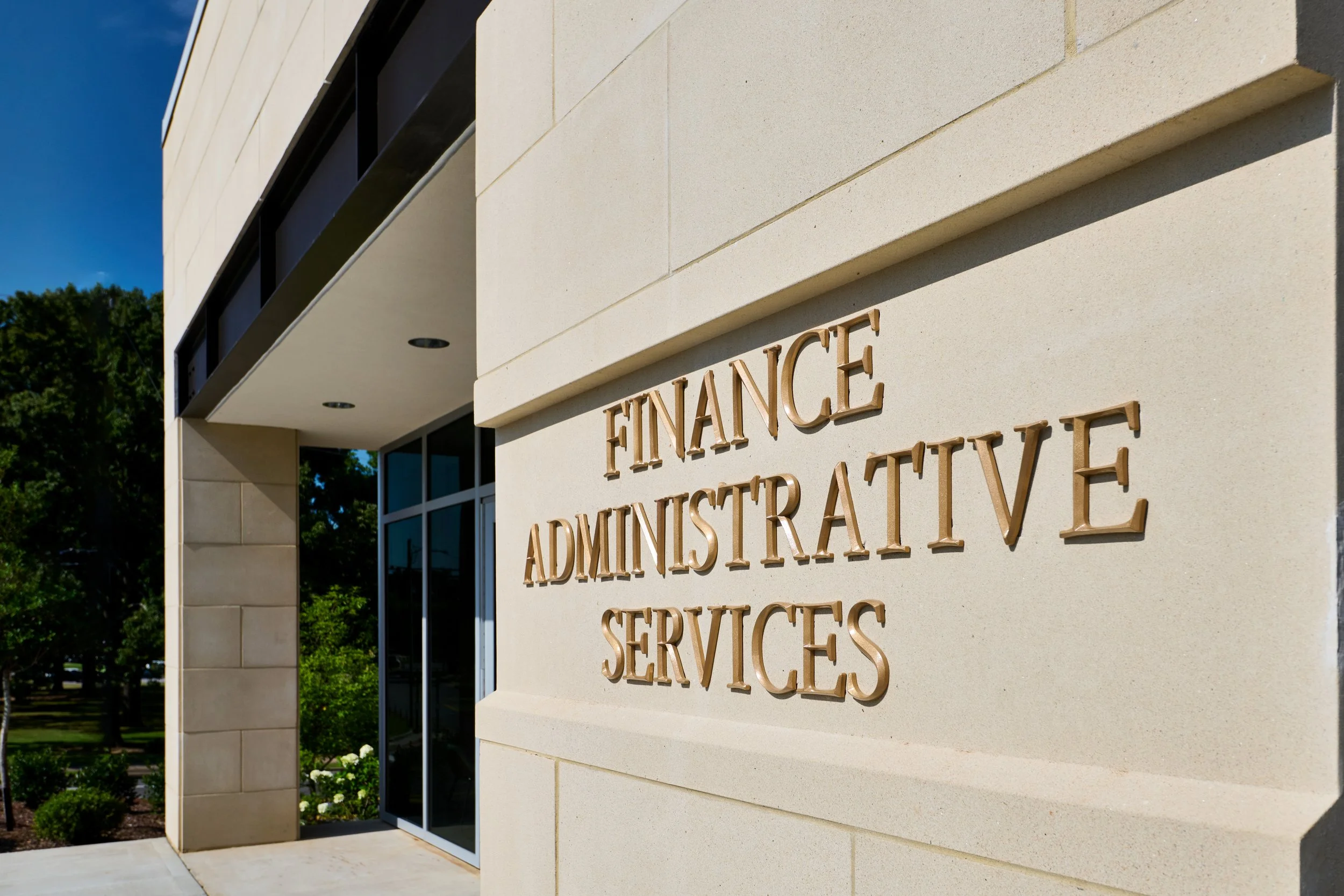 Exterior of a University building with a sign that reads 'Finance Administrative Services' on a cream-colored cast stone wall-project by B Group Architecture, Inc.