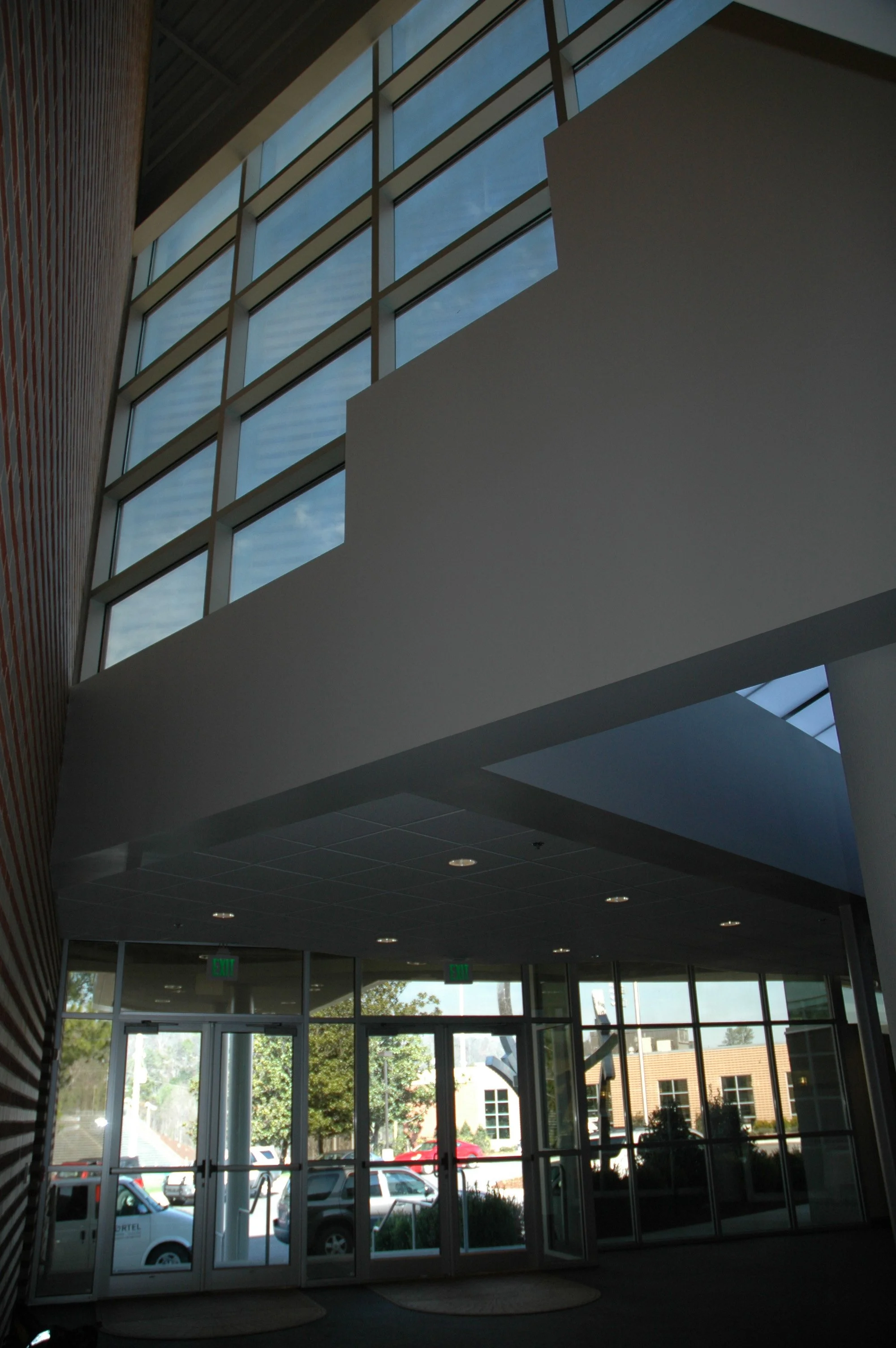 Interior view of a modern building with large glass windows, a high ceiling, and entrance doors. -project by B Group Architecture, Inc.