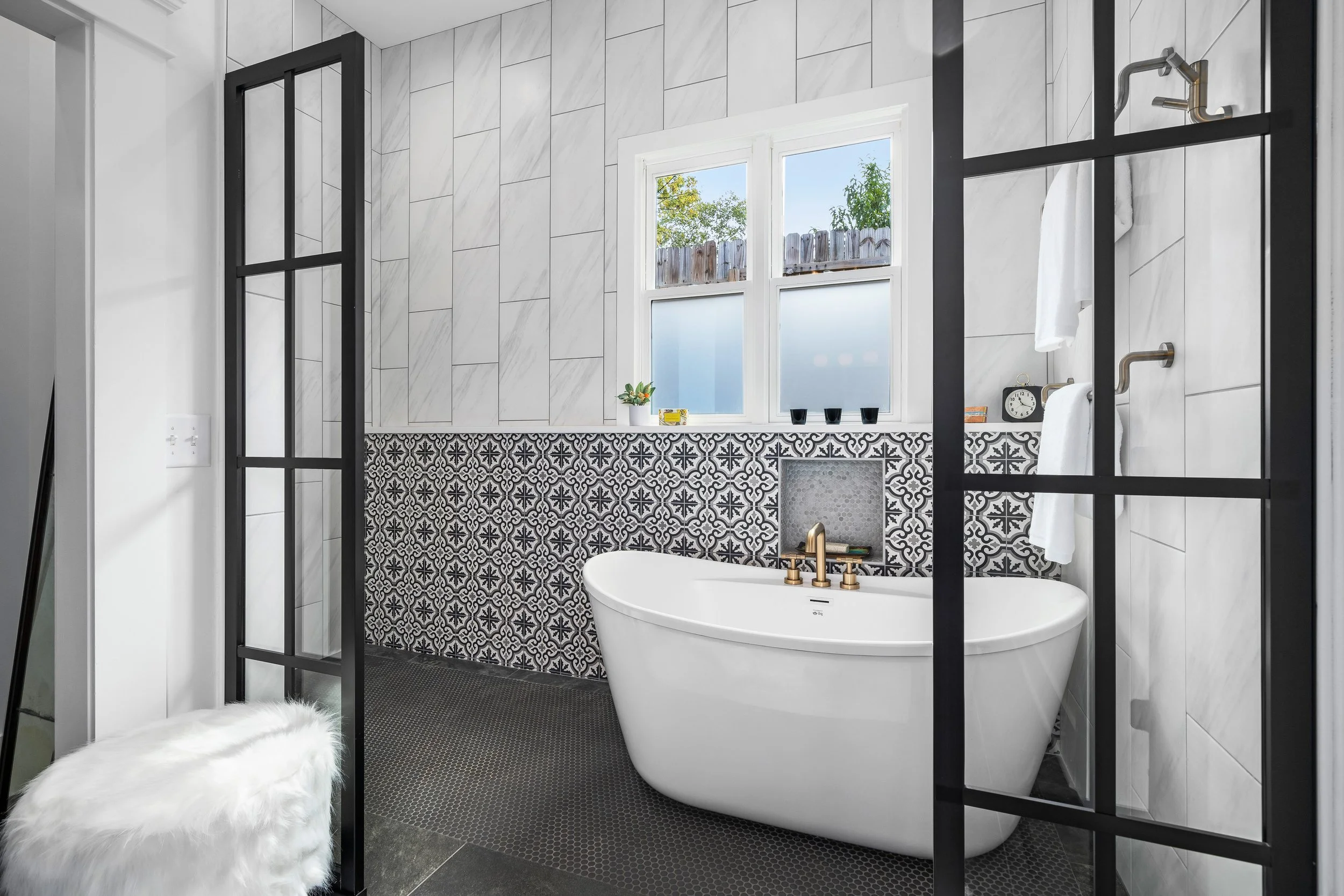 Modern shower with a white freestanding bathtub, patterned black and white tile wall, marble tile walls, black-framed glass partition, window with frosted glass. project by B Group Architecture, Inc.