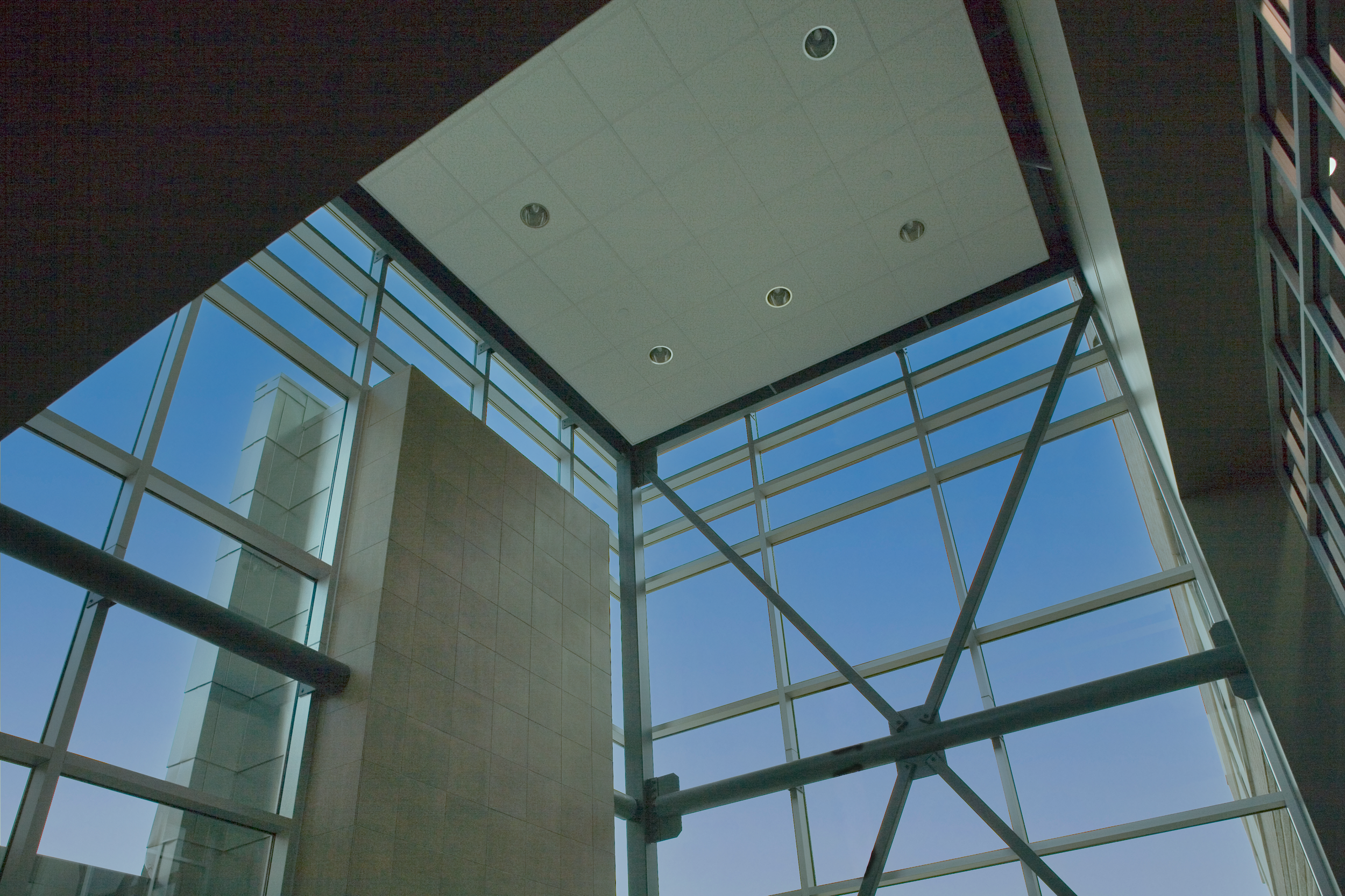 Interior view of a modern building with large glass windows and a high ceiling, showing blue sky outside. project by B Group Architecture Inc,