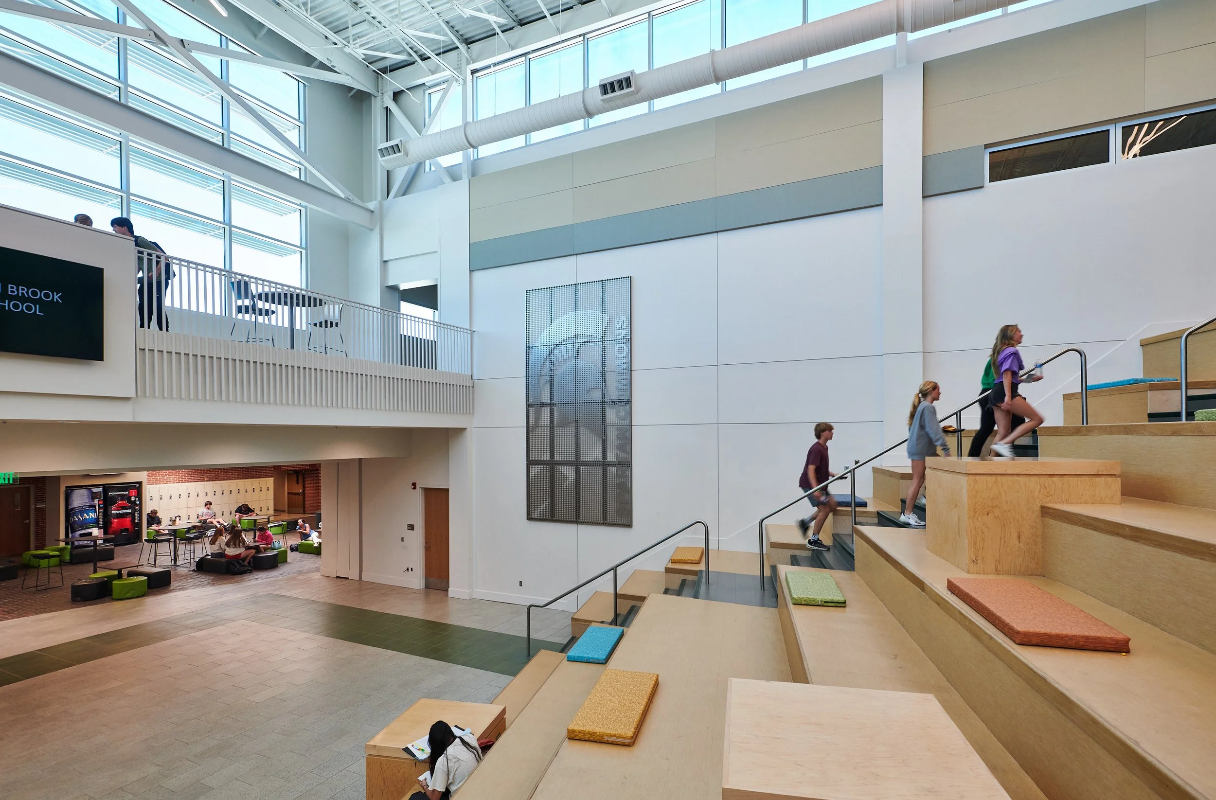 Interior view of a modern High School with the tiered cushioned seating and stairs  showcasing large clerestory insulated windows and exposed structure- project by B Group Architecture, Inc.