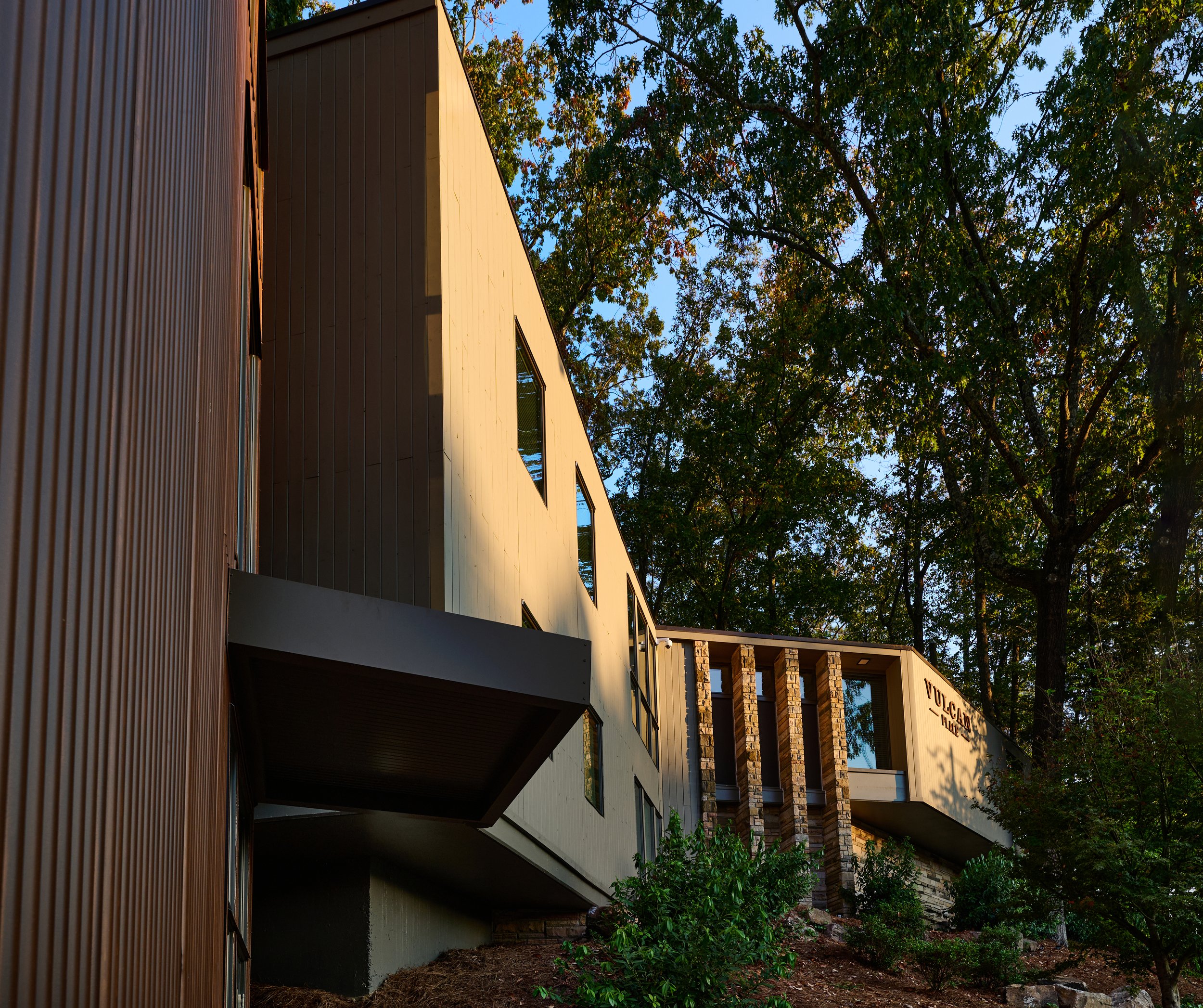 Modern multi-story building with large windows, surrounded by trees and greenery, with a sign that reads 'VULCAN PLACE' on the upper part of the facade.
