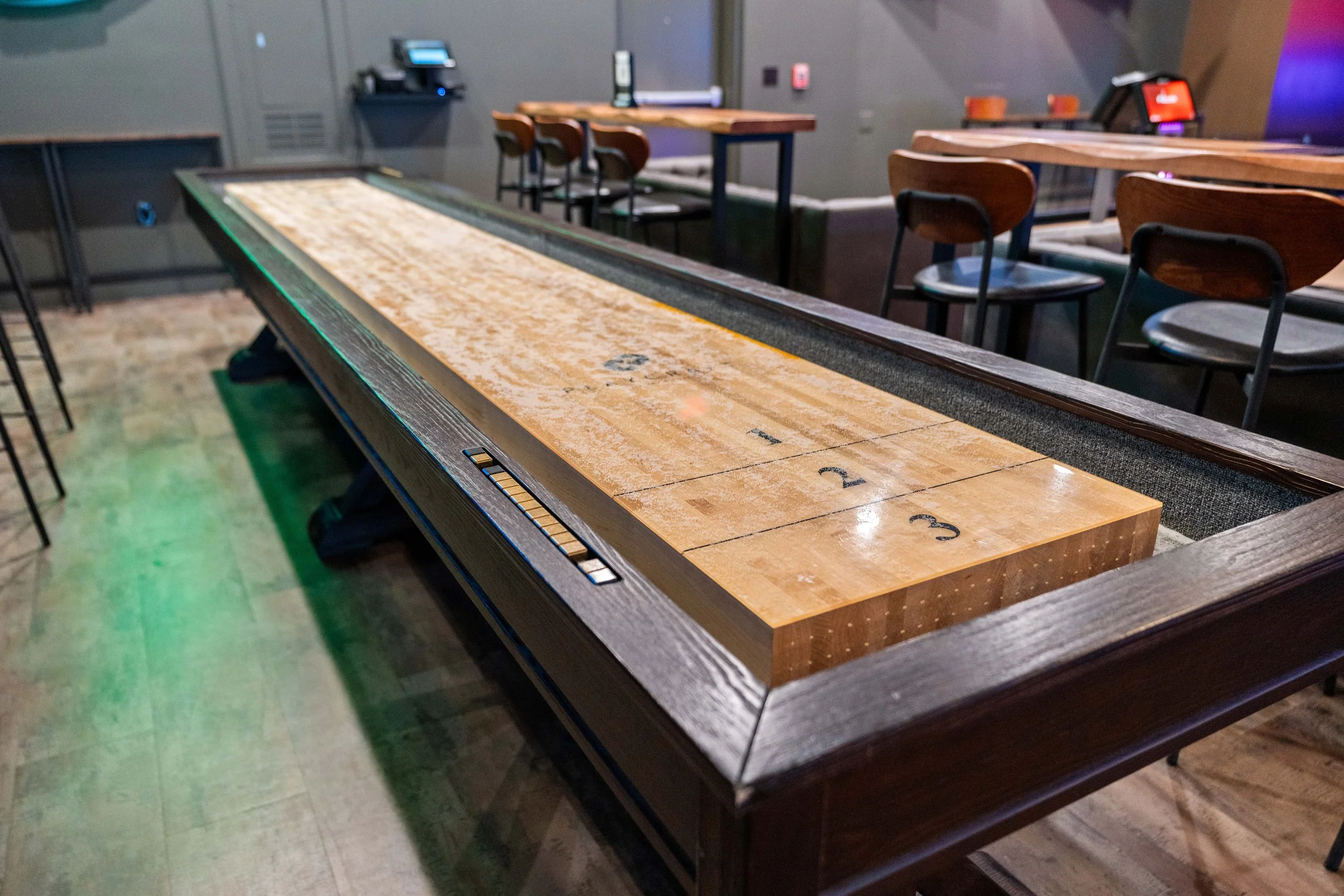 Shuffleboard table at Tap Ins sports bar with wooden chairs and tables in the background. project by B Group Architecture, Inc