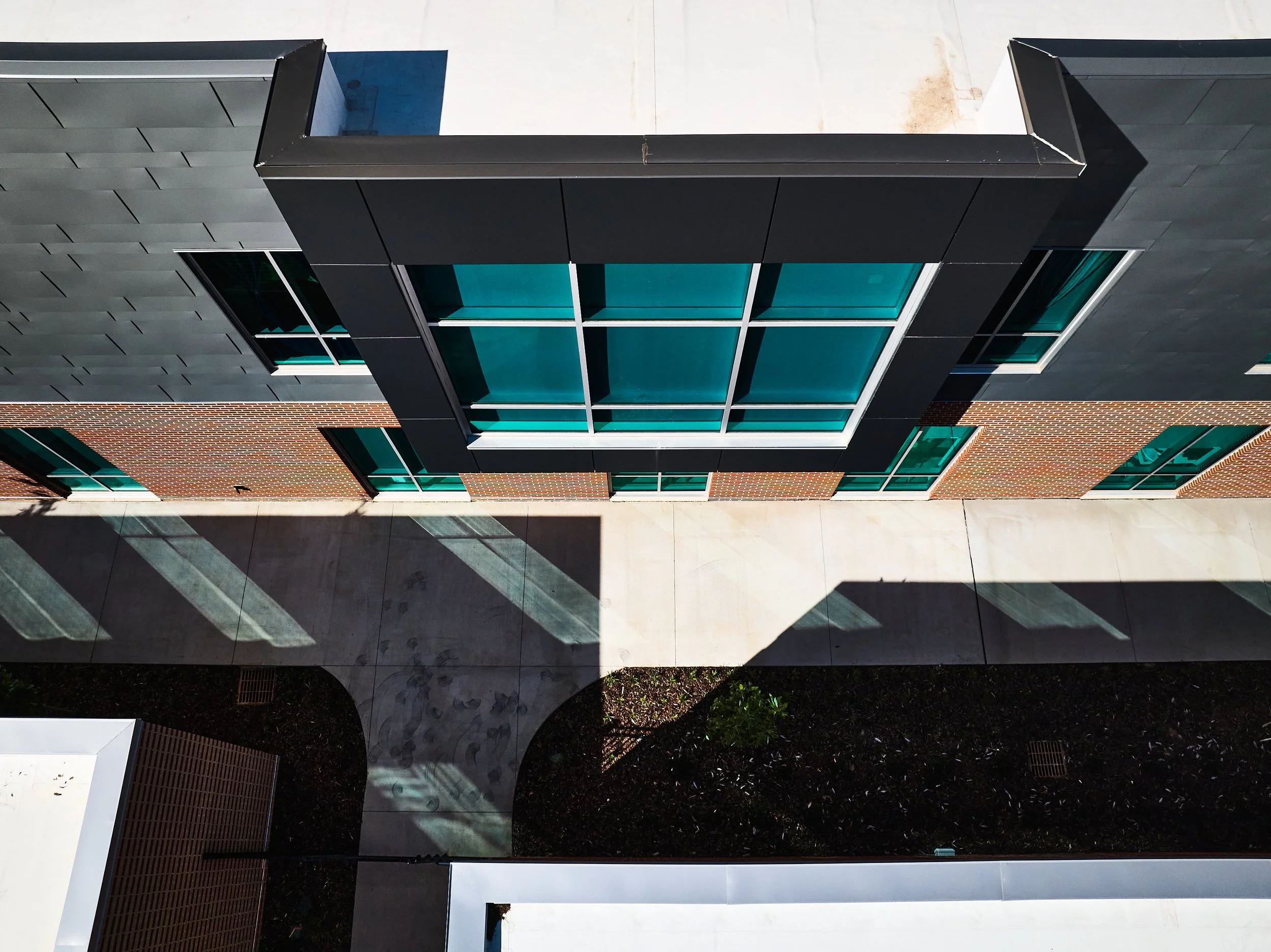 Looking down at the exterior of a modern building with custom metal panels and and brick facade and large glass windows- project by B Group Architecture, Inc.