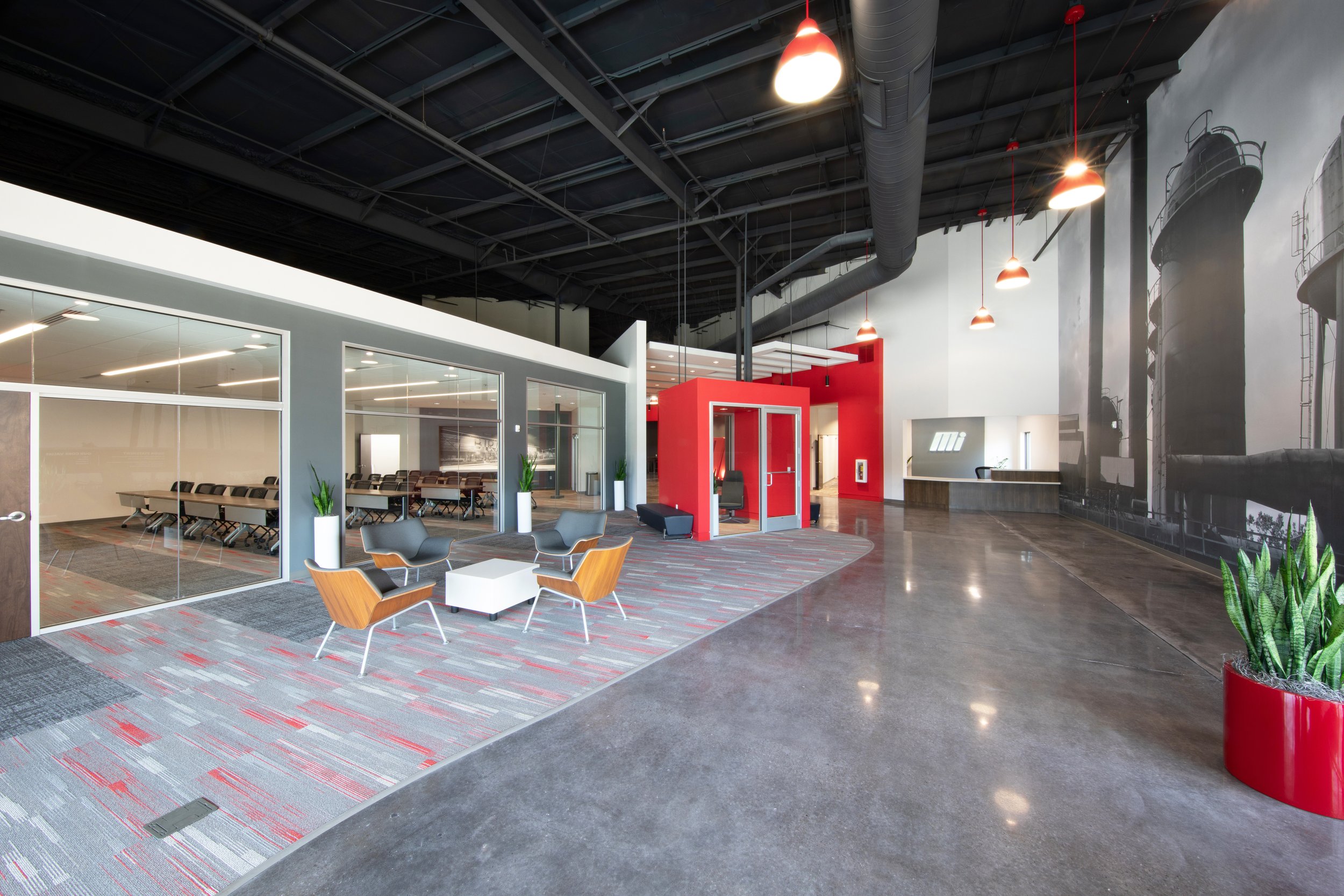 Modern corporate lobby with seating area, conference room with glass walls, and mural of industrial silos on the wall. Highlighted by Motion Industries signature red accent color.  project by B Group Architecture, Inc. 
